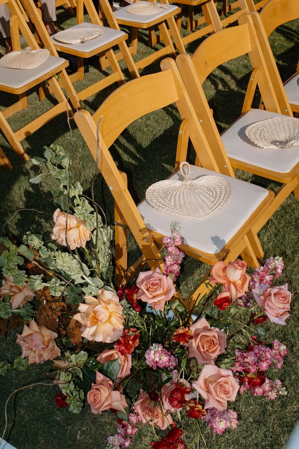 wedding ceremony chair with rattan fans and lush pink, peach aisle florals