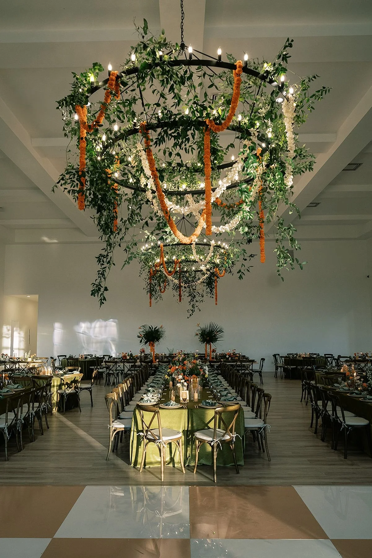 Tan and white checkered dance floor of a retro, tropical, cultural fusion wedding reception with greens and strands of marigolds draped from chandelier at the Arlo wedding venue north of austin texas