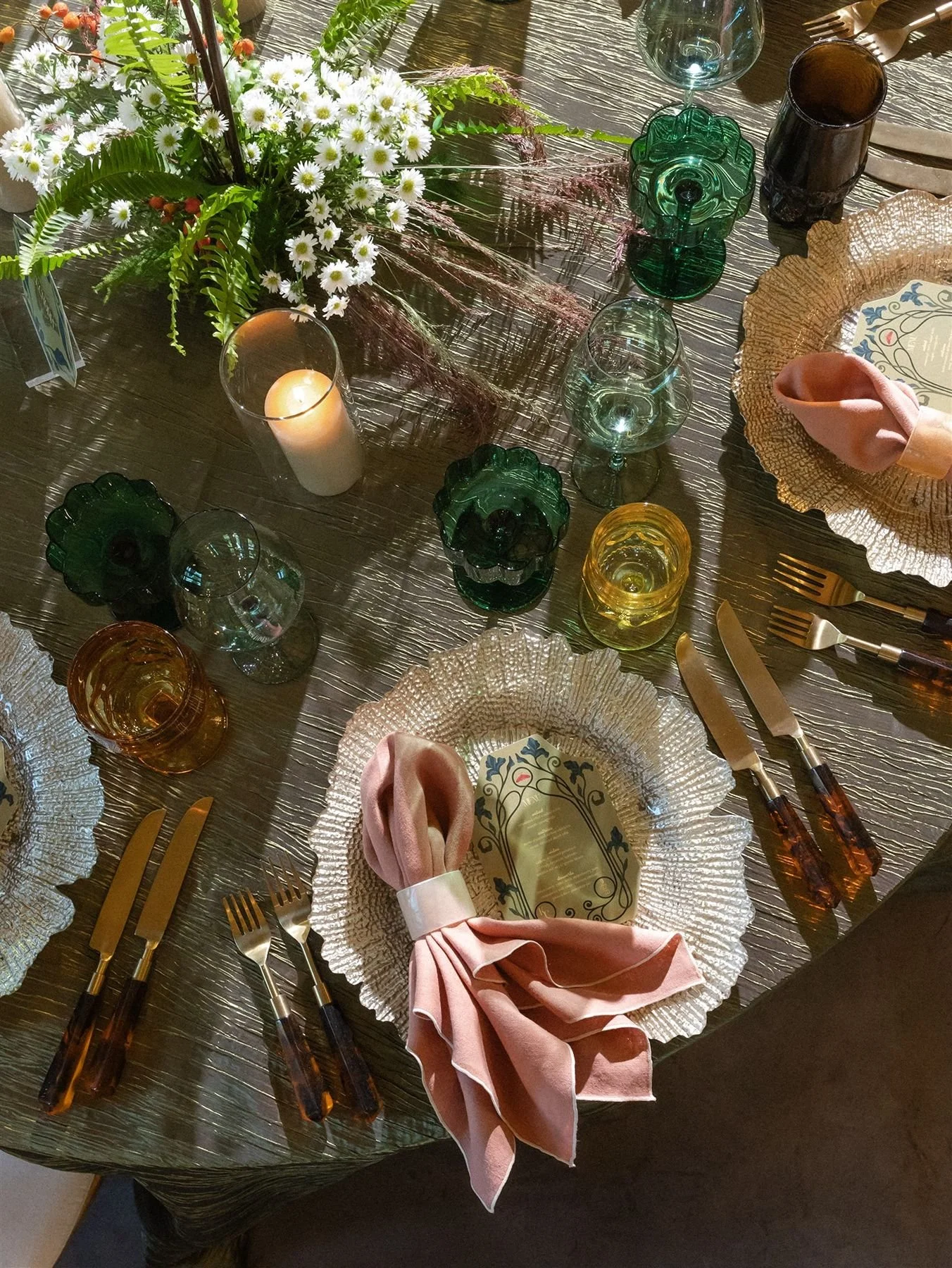 Raw edges ribbed champagne chargers on textured olive green linens with jacquard flatware and custom glassware with mismatched gold glasses and scalloped green coupes and wildly organic green centerpieces 