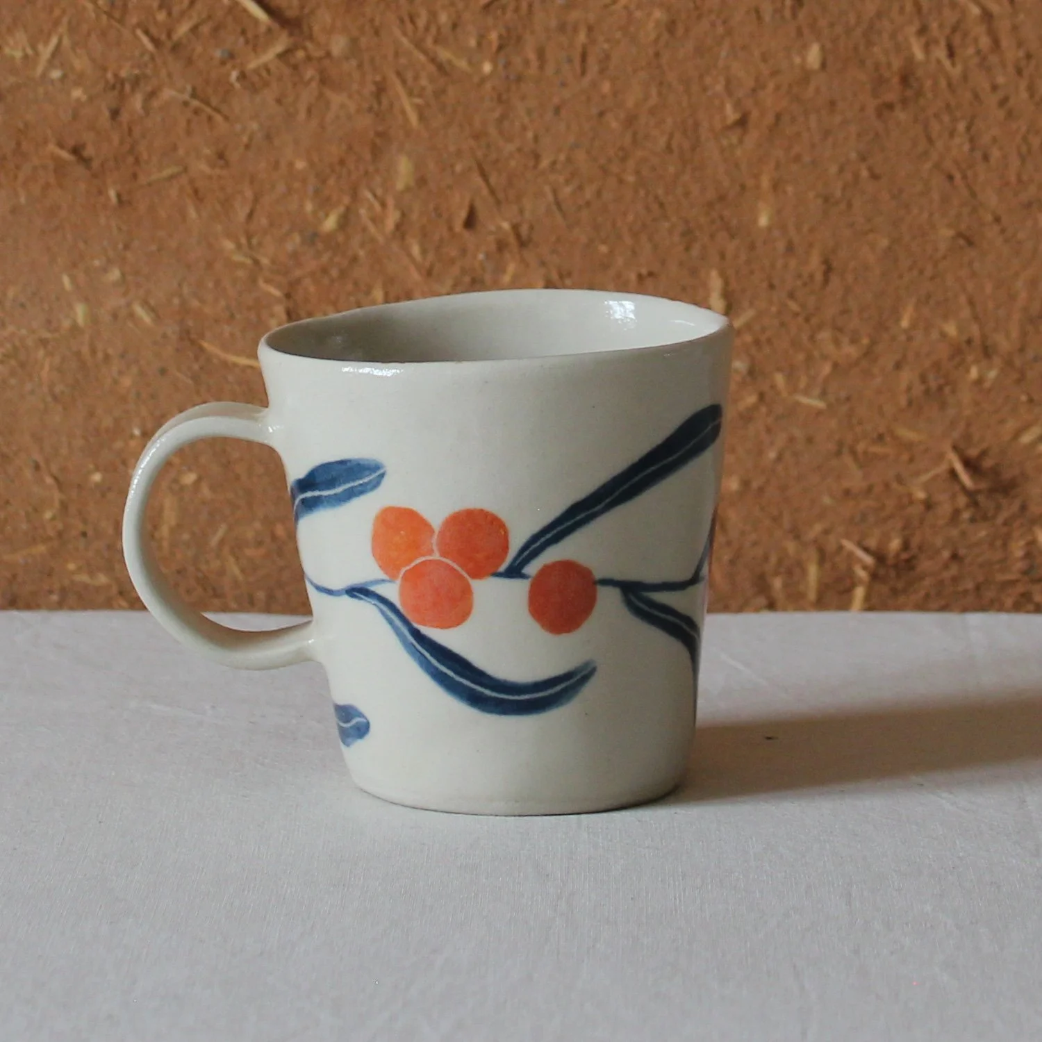  Vue de profil d’une tasse à anse conique à base étroute, en grès, motif Argousier, création artisanale à Nanteau-sur-Lunain 