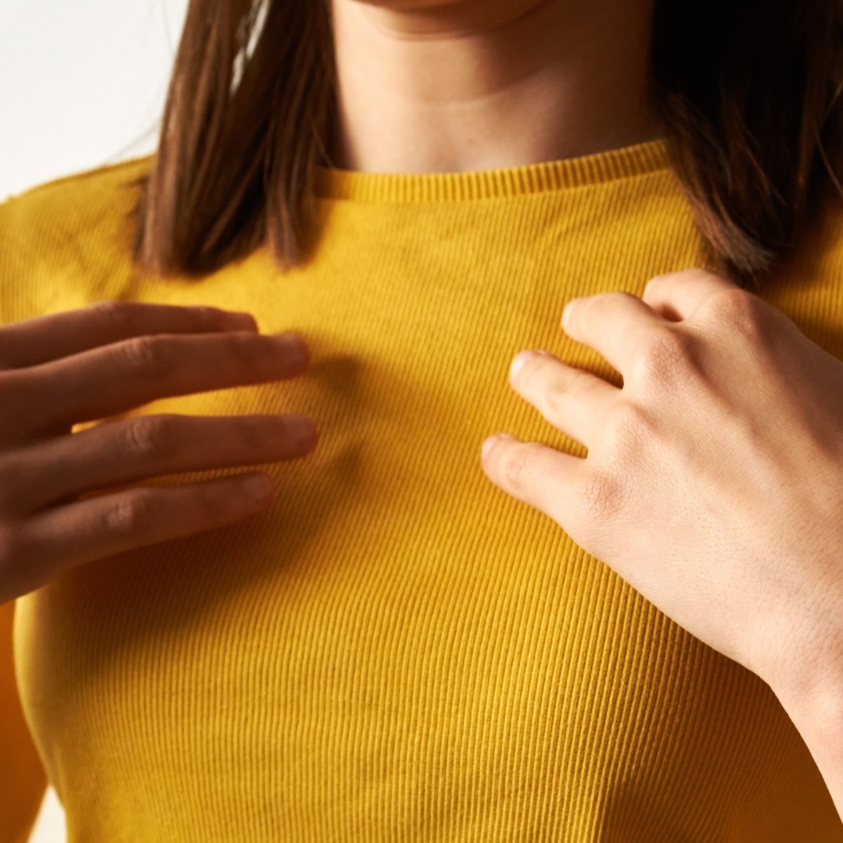 Close-up of a person wearing a mustard yellow ribbed top, with hands gently touching the chest area.
