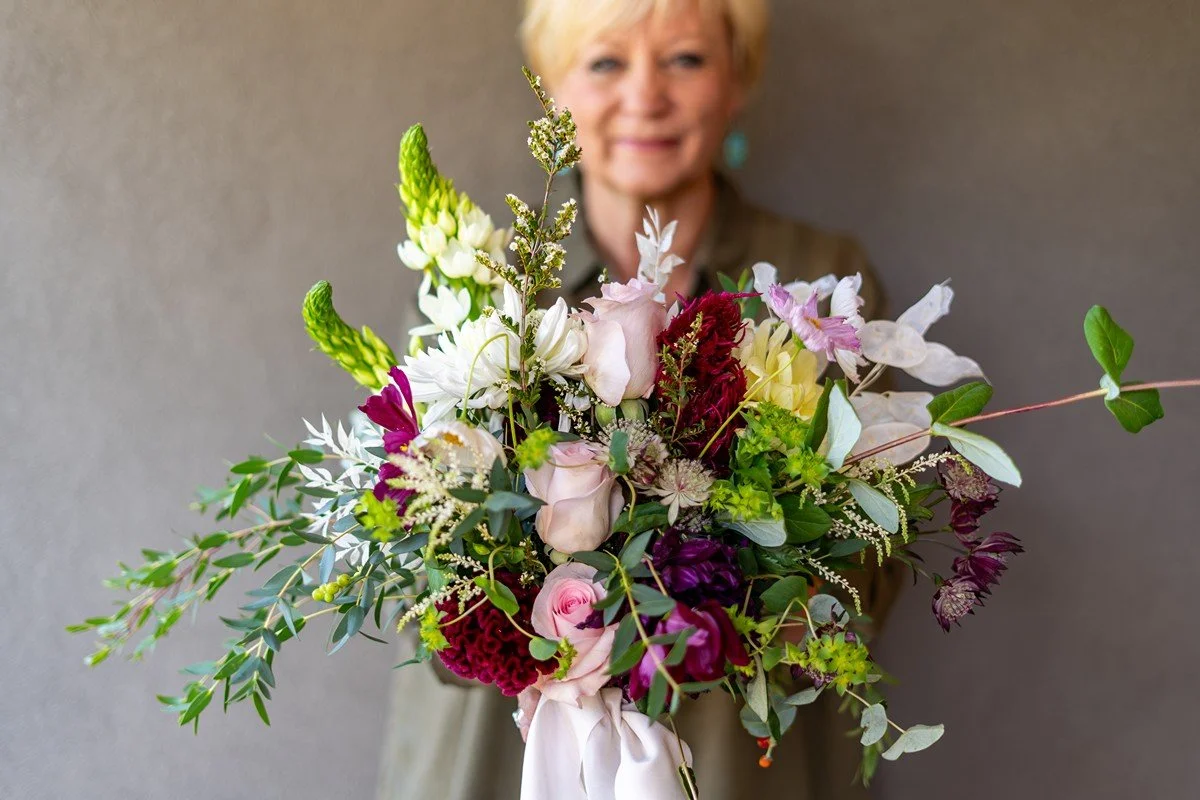 A woman holding a large bouquet of multicolored flowers with a blurred background.