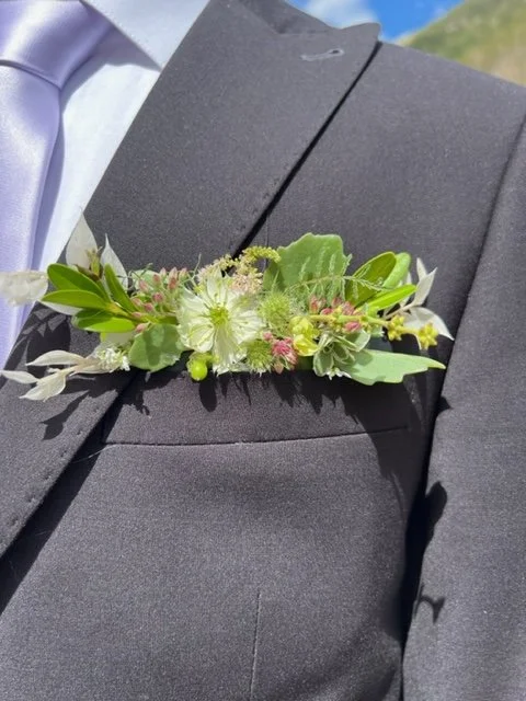 A boutonniere with white and pink flowers and green leaves worn on a dark gray suit jacket.