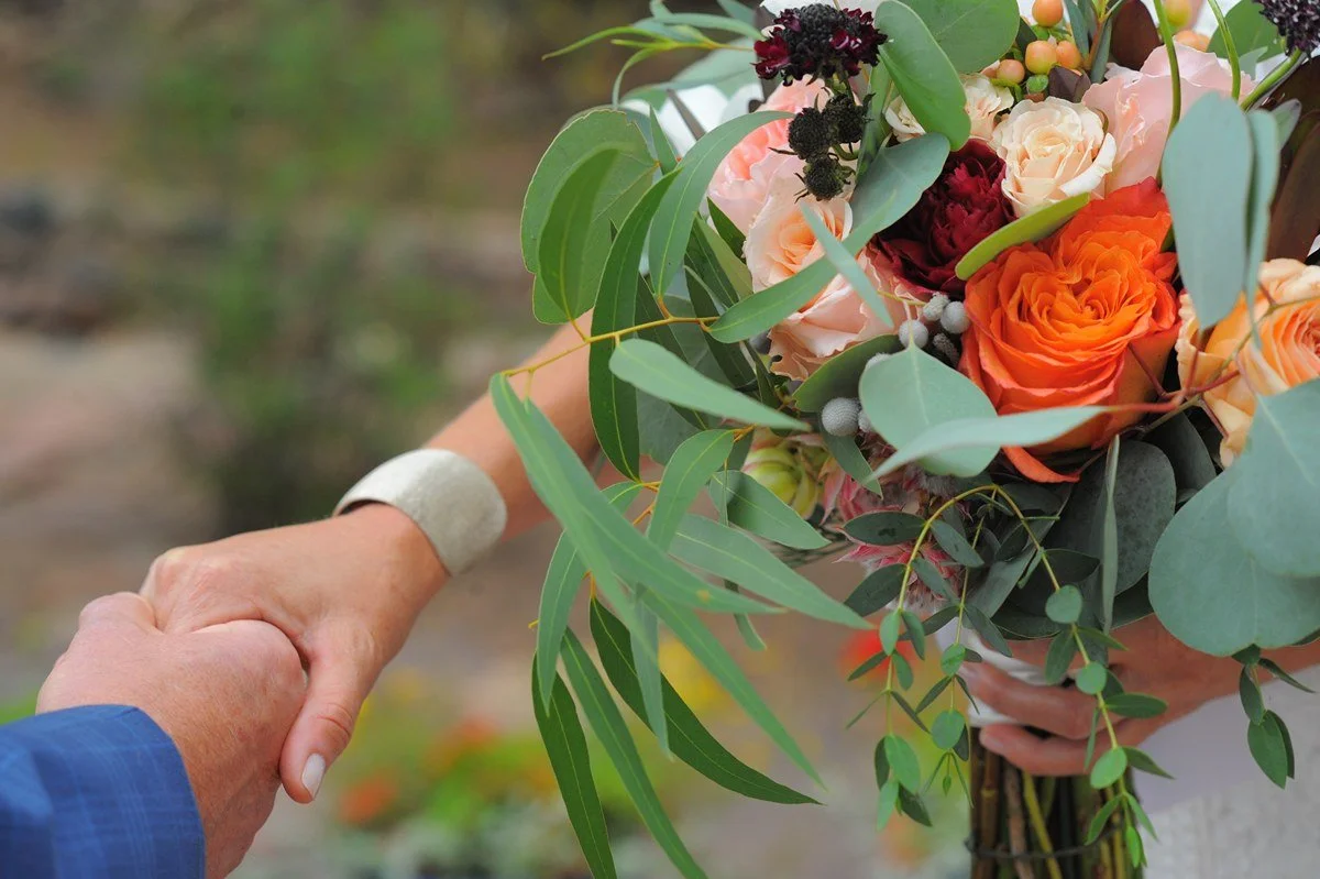 A person holding hands with another person who is holding a bouquet of mixed flowers and greenery.