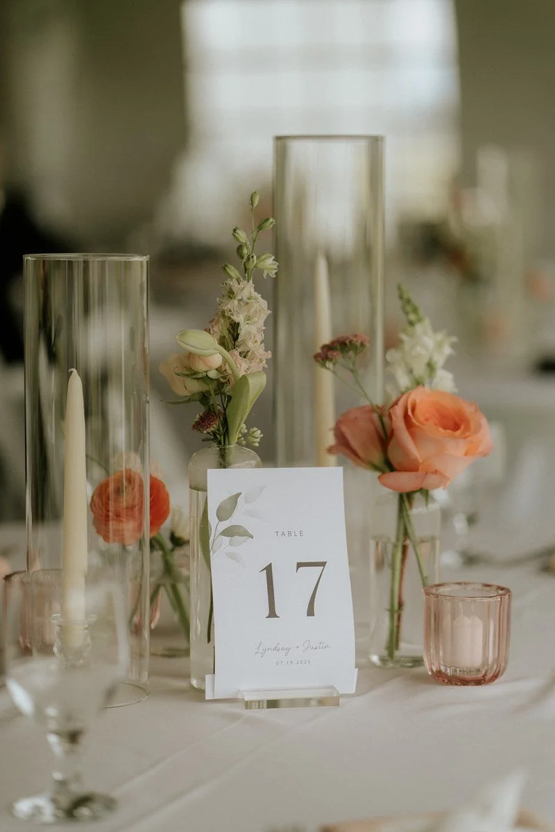 Elegant wedding table decoration with floral arrangements, candles, and a table number sign reading '17' with names Lindsay and Austin and the date 07.19.2025.