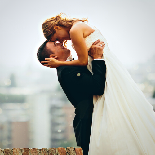 Bride and groom embracing on a rooftop with cityscape background.