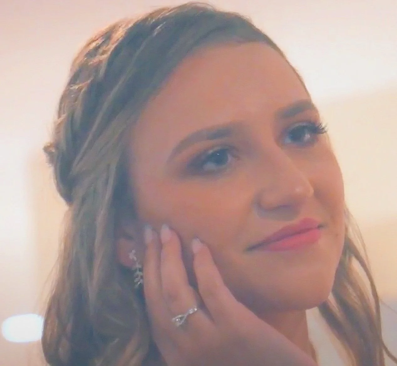 Smiling person with braided hair and an earring, resting hand on face