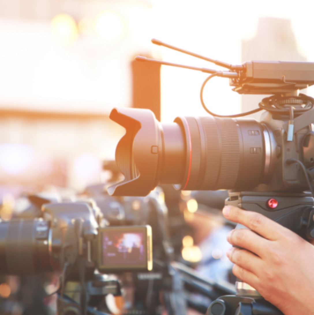 Close-up of professional video camera with person operating it, outdoors with bright sunlight.