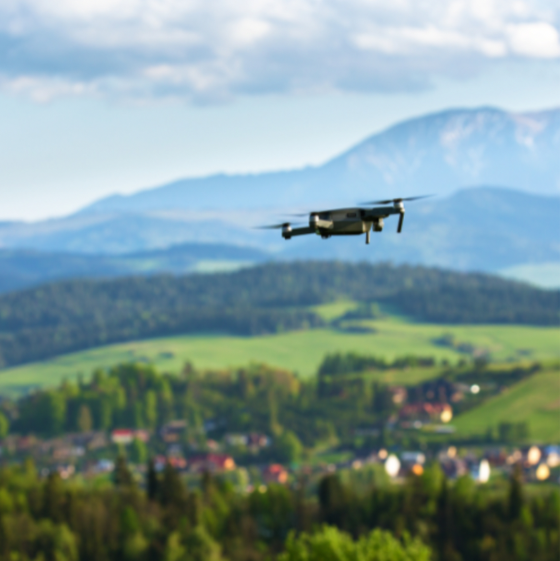 Drone flying over a scenic landscape with hills and a village, under a cloudy sky.