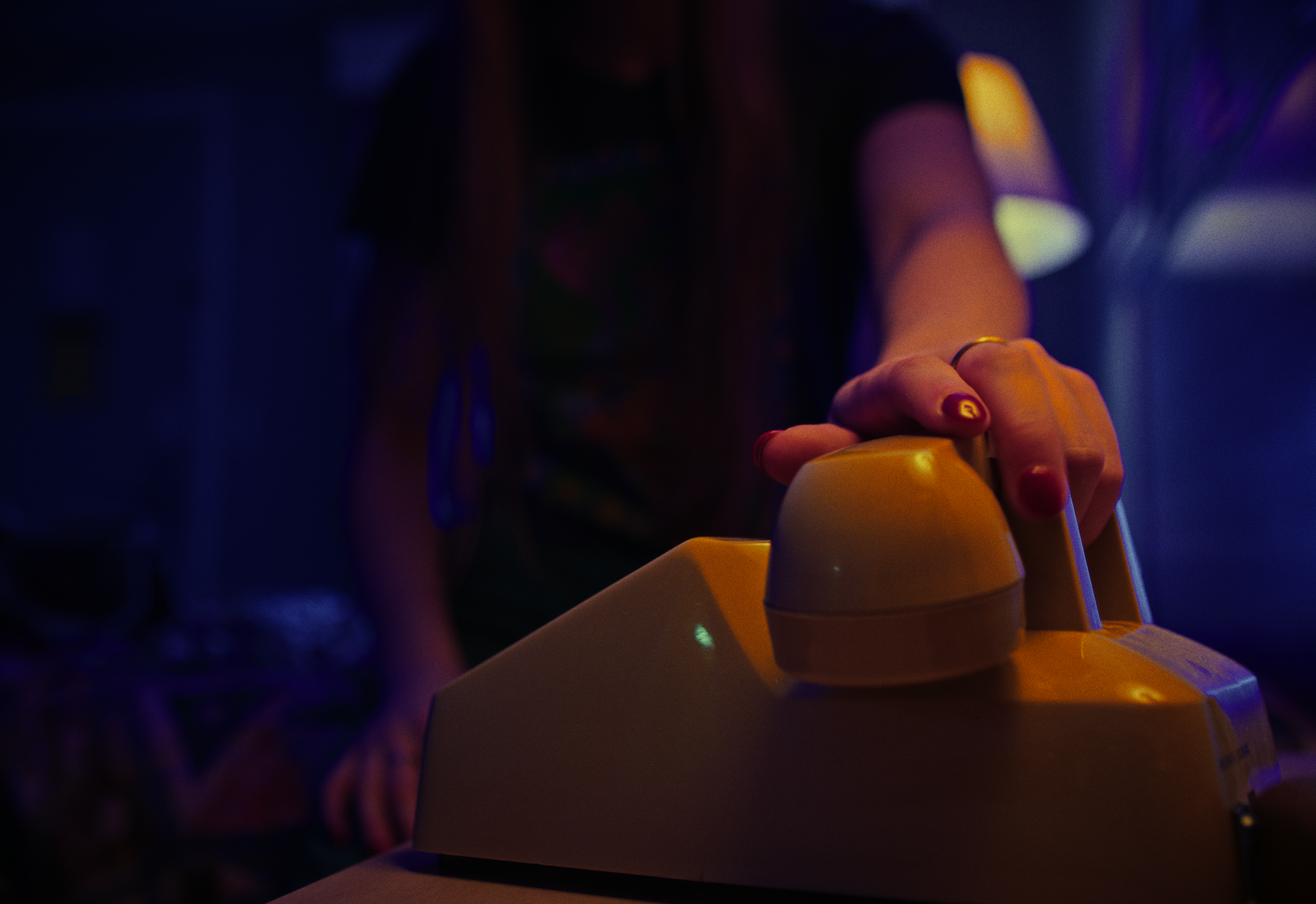 A person pressing a yellow button on a yellow device, with a dark background and dim lighting.