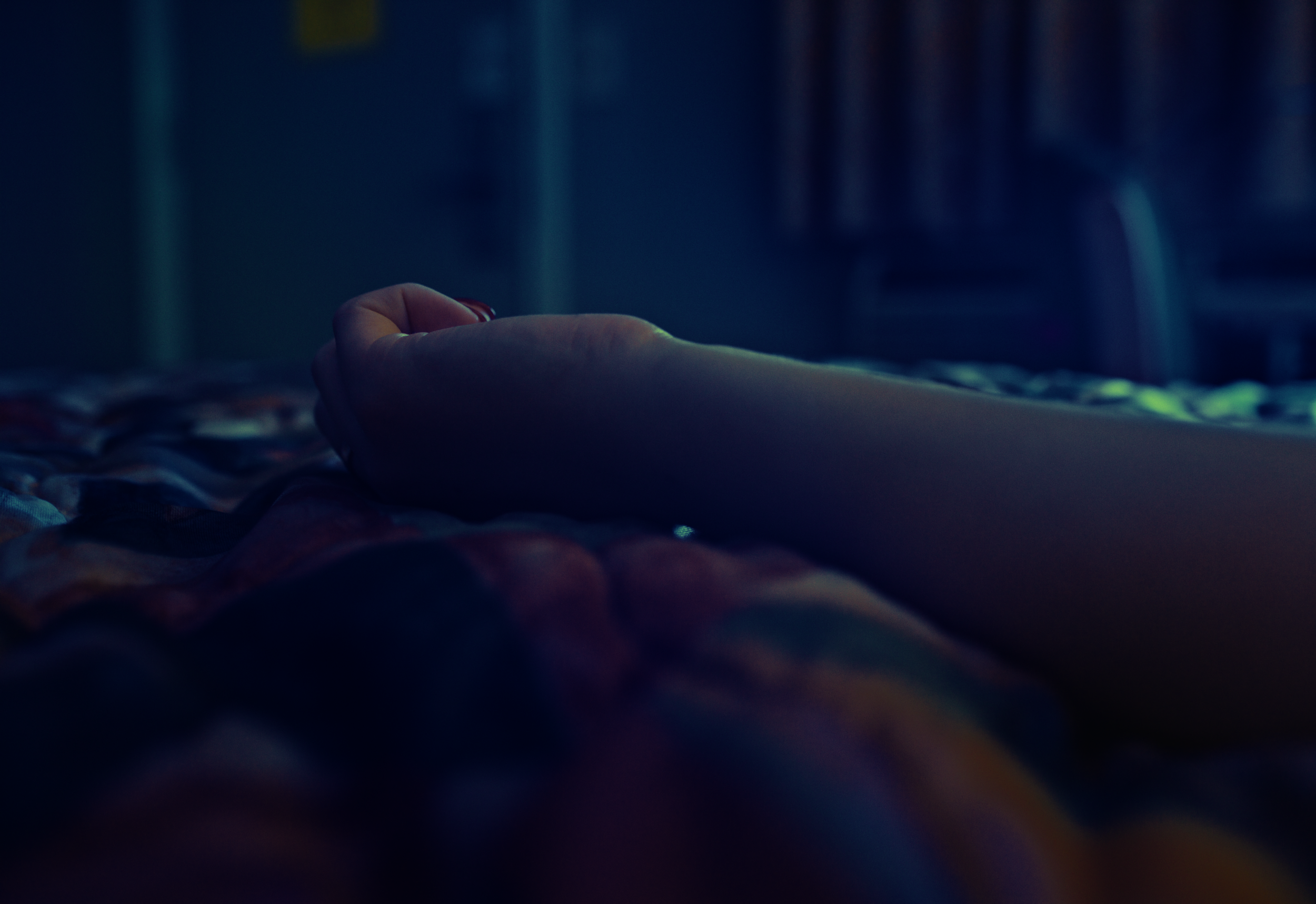 A hand resting on a colorful quilt in a dimly lit room.