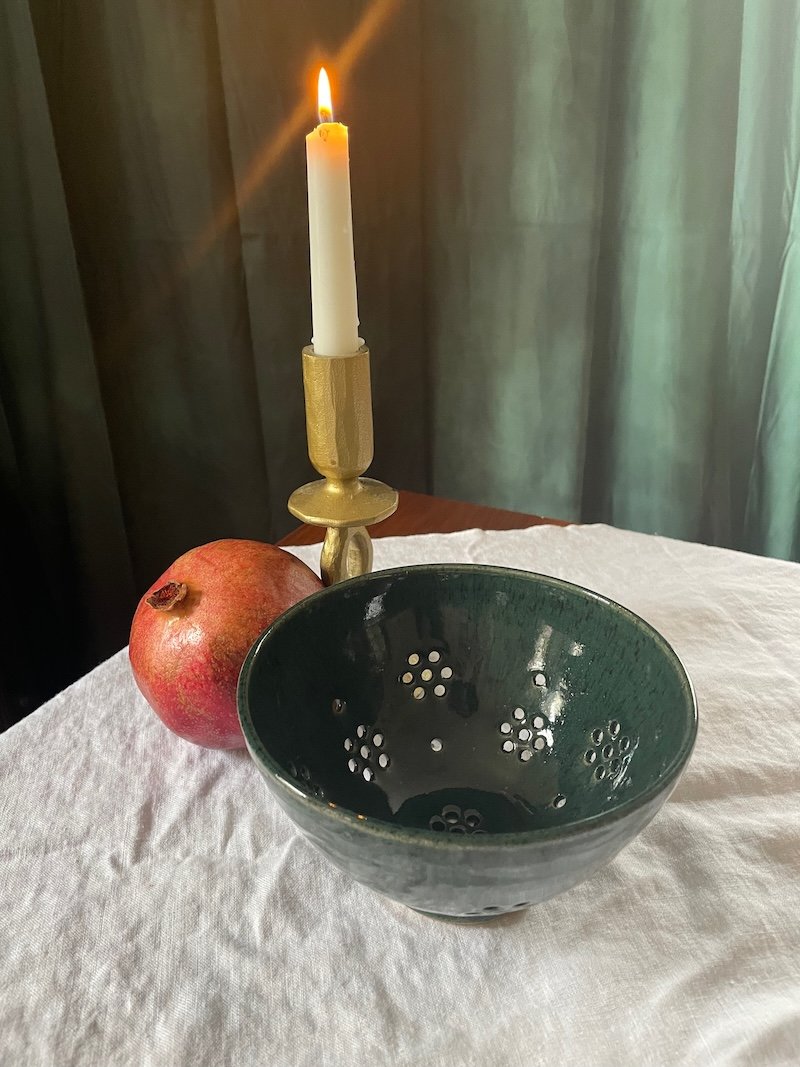 Dark green berry bowl before a pomegranate and a lit candle, Richmond pottery
