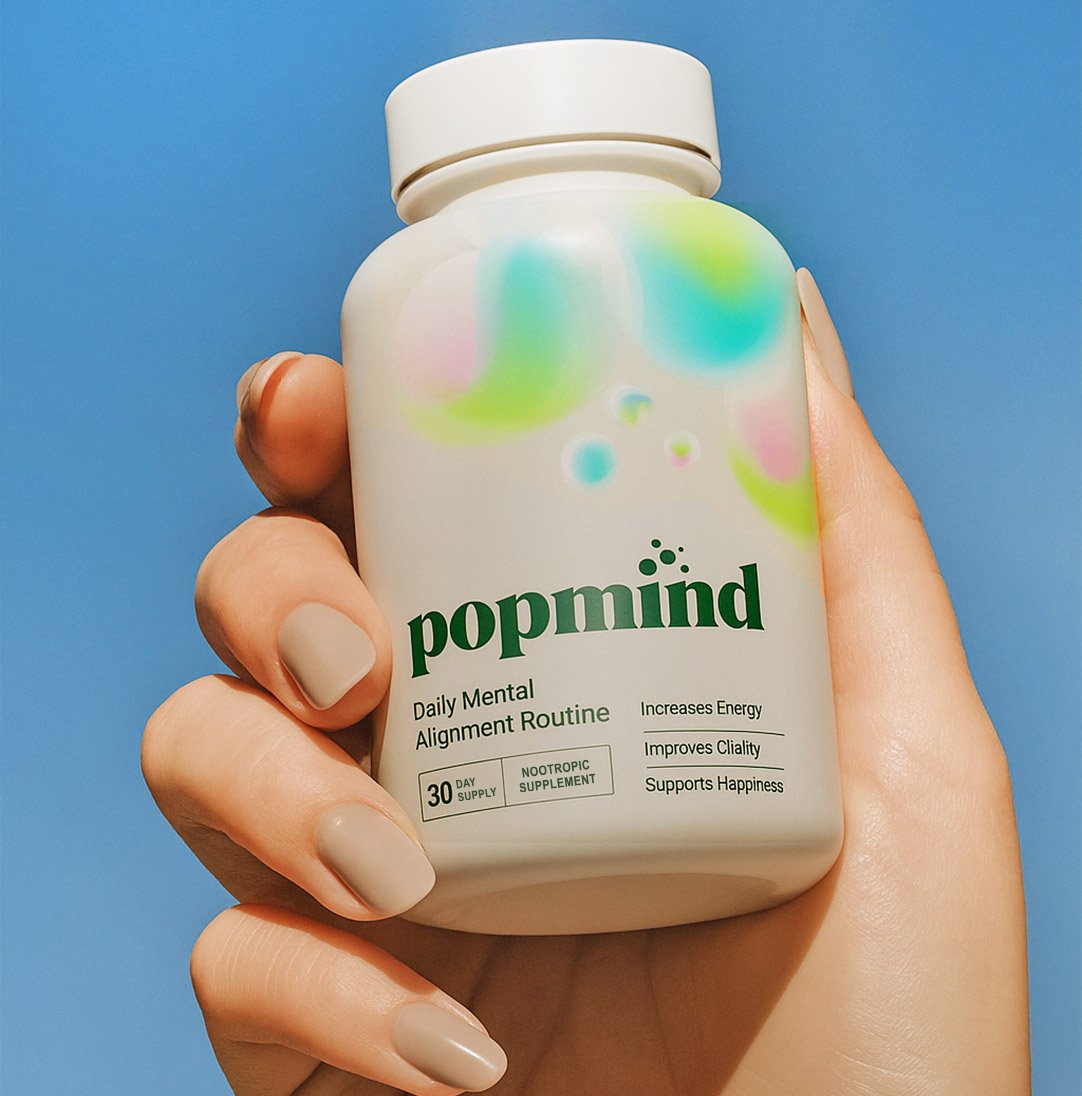 A hand holding a bottle of PopMIND dietary supplement against a blue background.