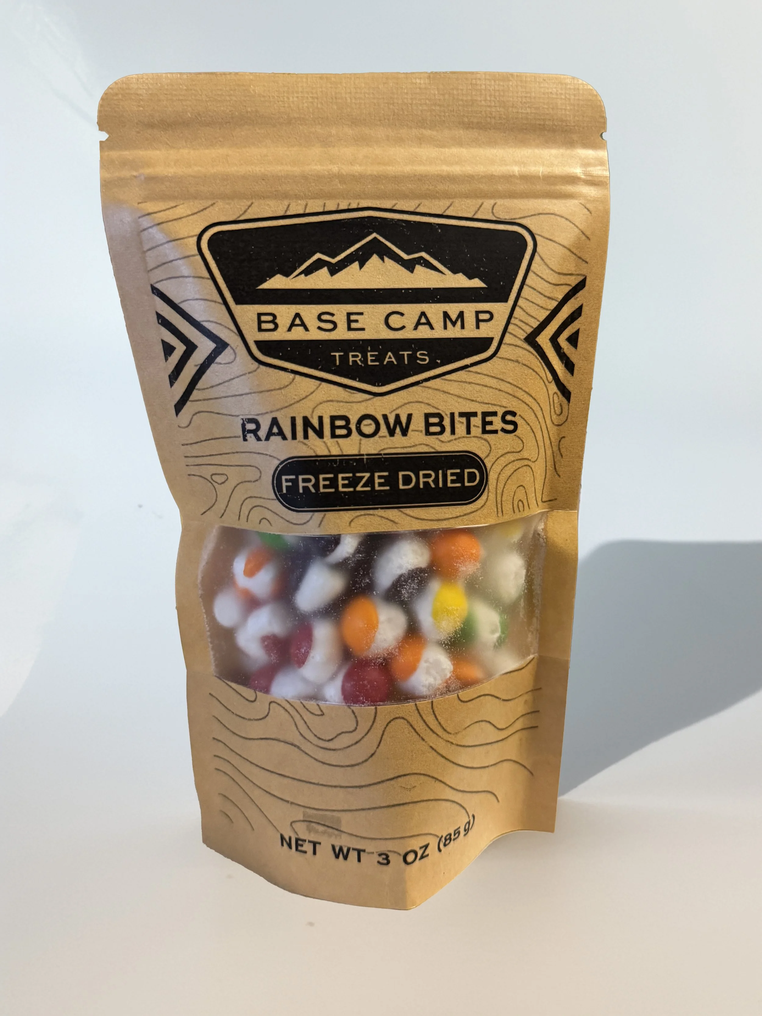 Base Camp Treats Freeze Dried Skittles in kraft stand-up pouch with colorful puffed rainbow candy visible through clear window.