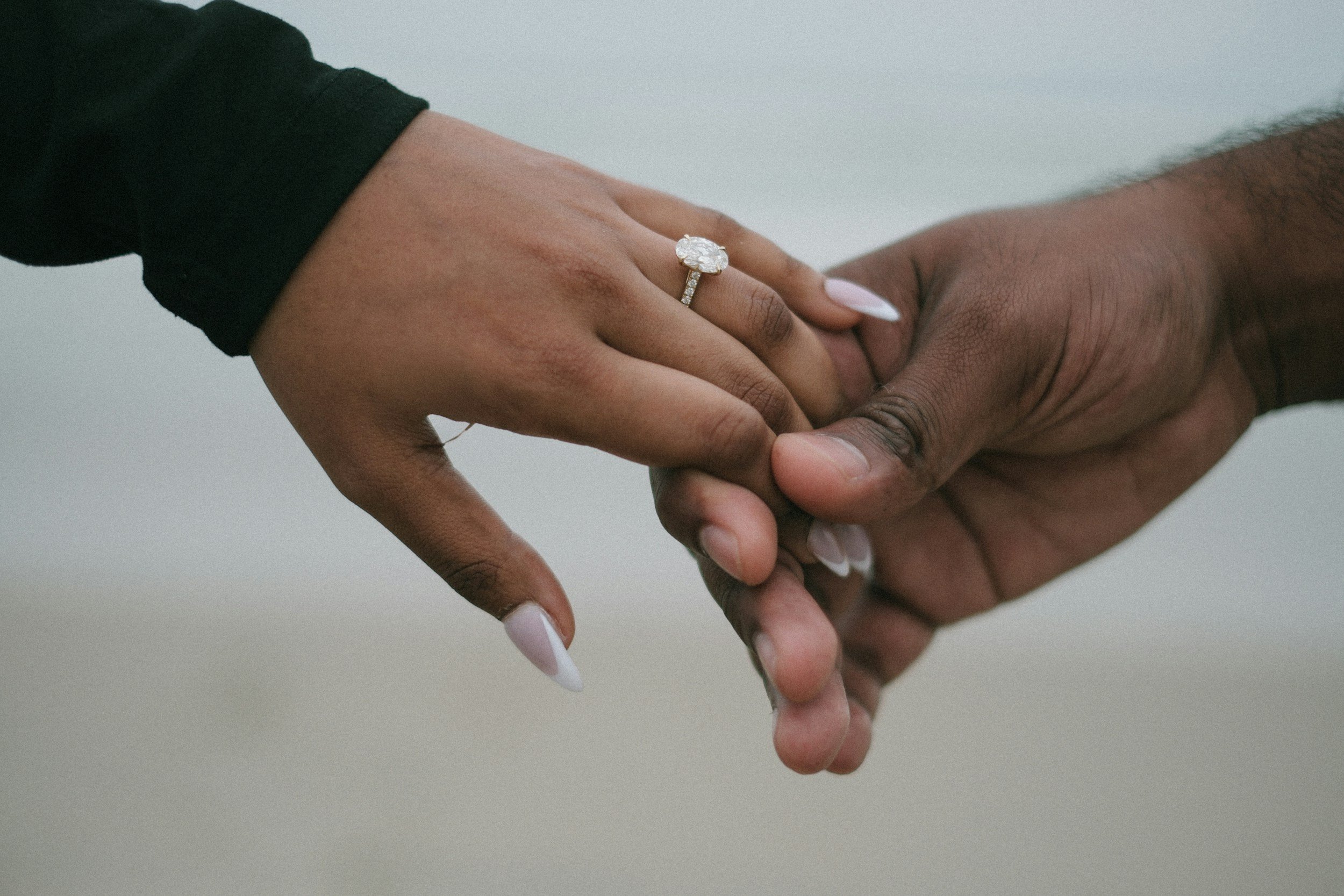 Close-up of a couple holding hands, one wearing an engagement ring with a large diamond.