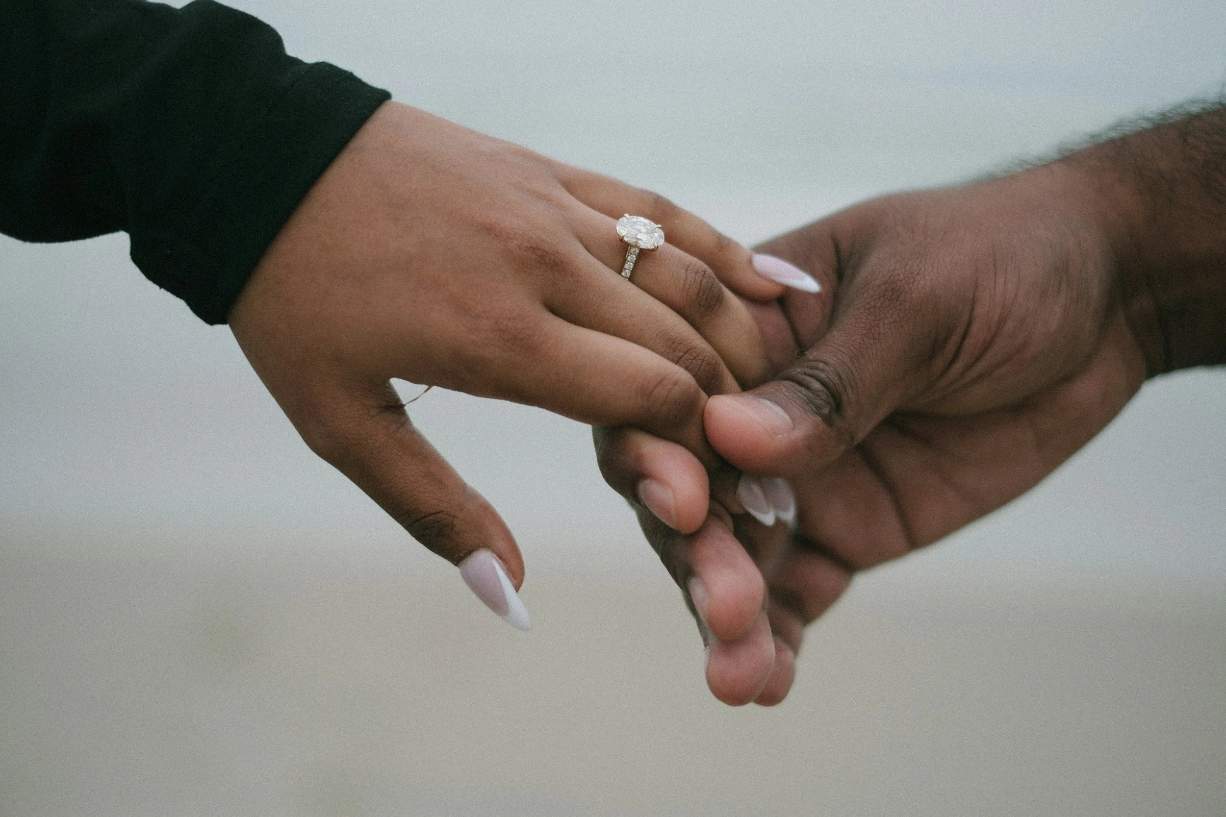 Two people holding hands with one person's hand having an engagement ring