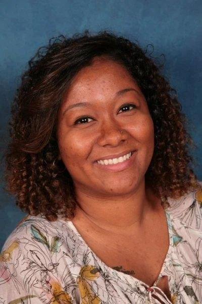 A woman with curly hair smiling at the camera against a blue background.