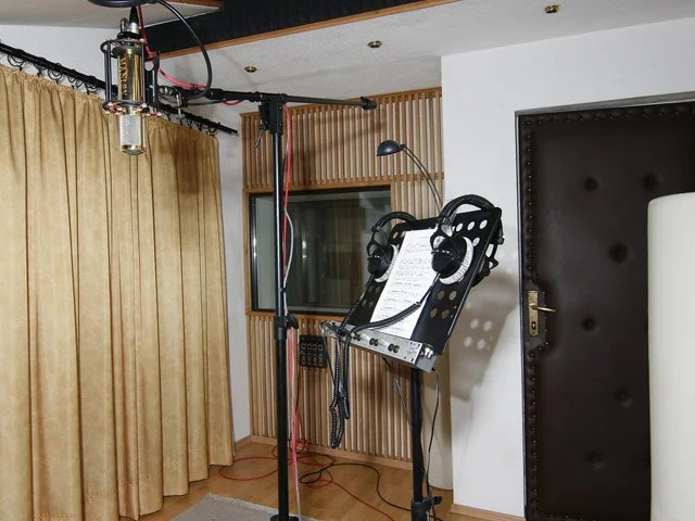 Music recording studio with microphones, headphones, and sound equipment in a room with wooden paneling and a window