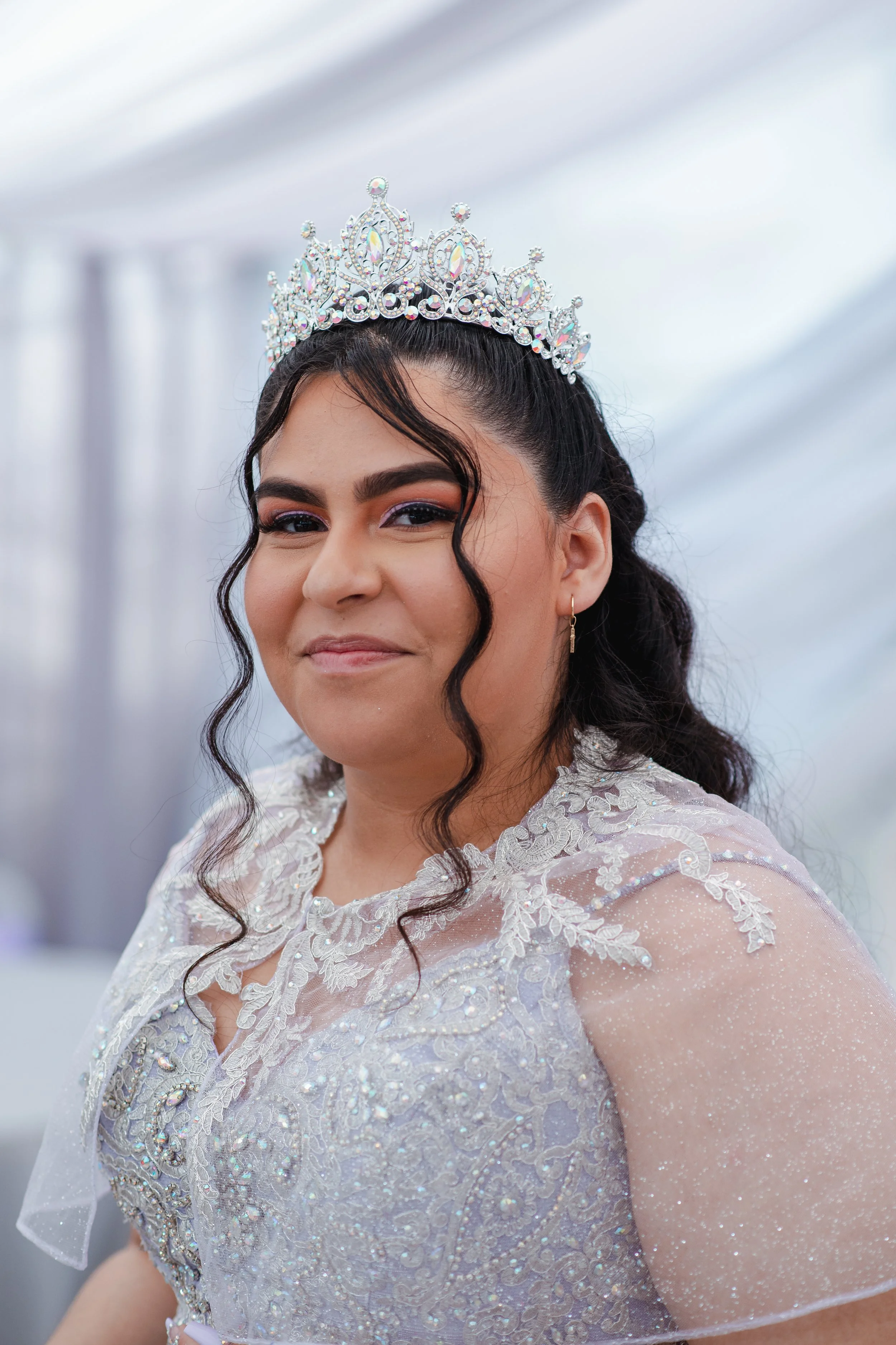 Close-up of a young woman wearing a silver tiara and a white dress with intricate embroidery and sparkling details. Quinceañera birthday celebration in Orange County.