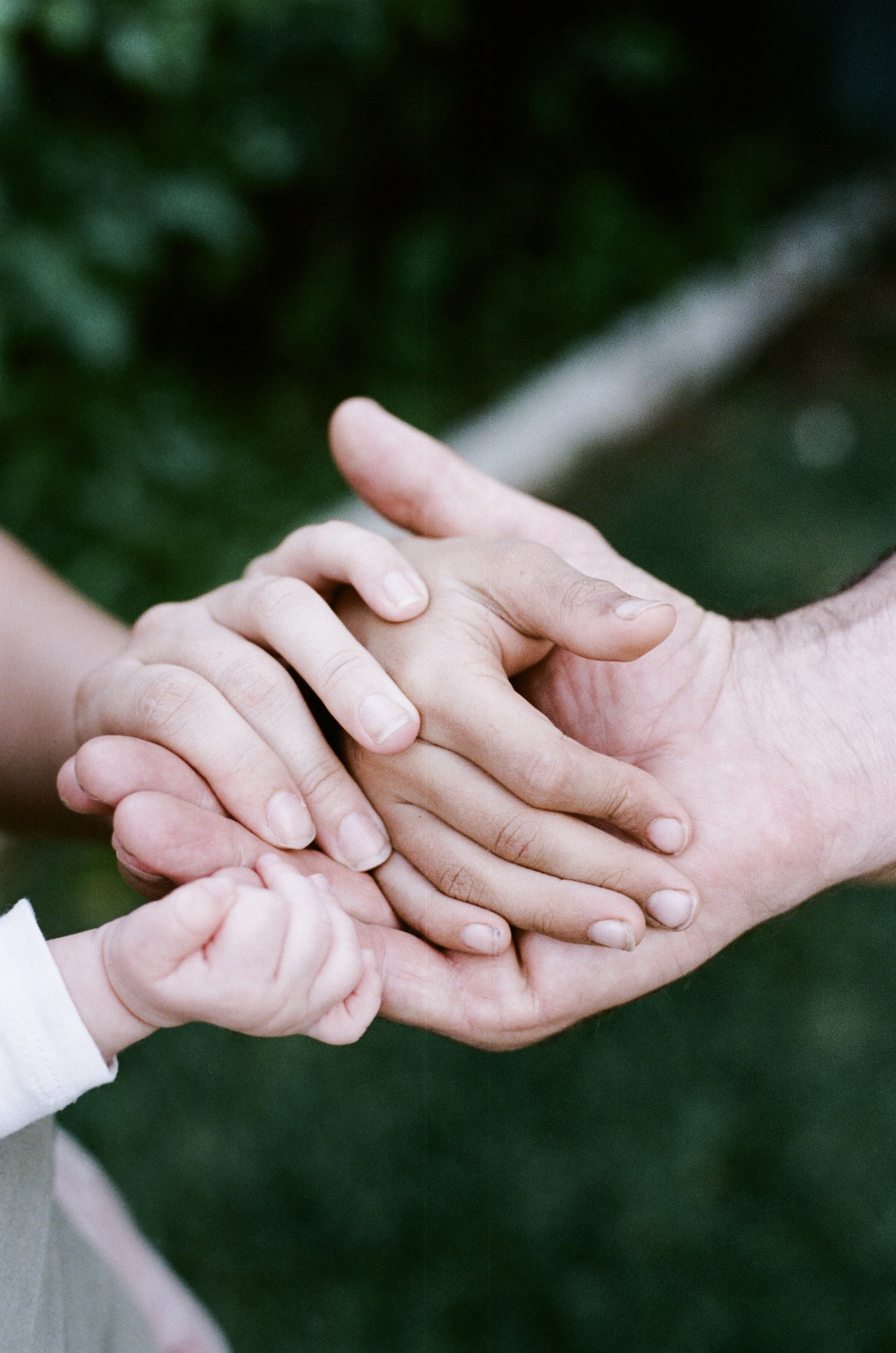 Close-up of multiple hands: an adult's hand holding a child's hand, with other children's hands surrounding them, indicating a gesture of support or care.