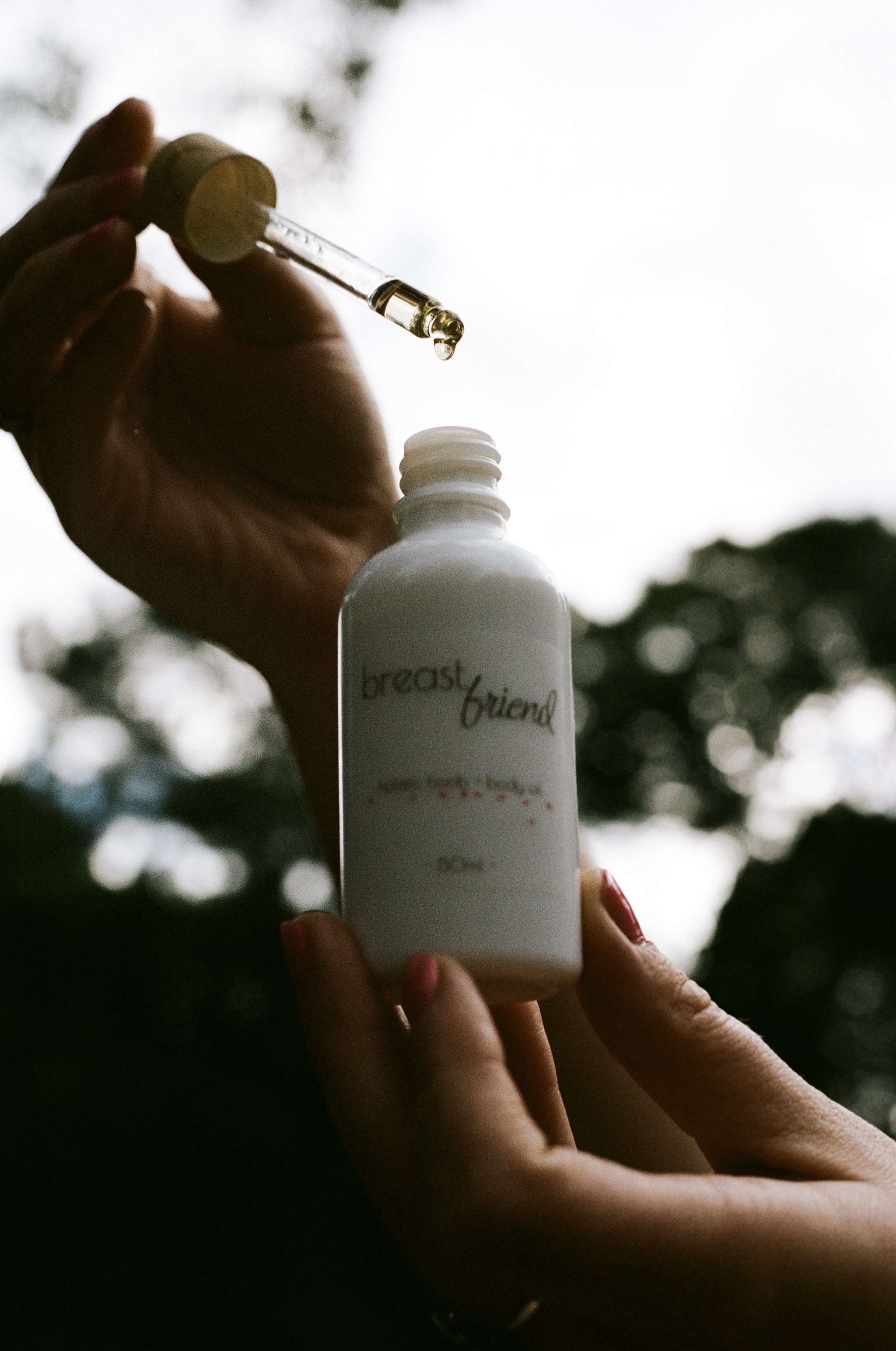 A person holding a white bottle labeled 'breast friend' and a dropper with a yellow liquid, possibly for breast milk storage or a medical purpose, against an outdoor background.