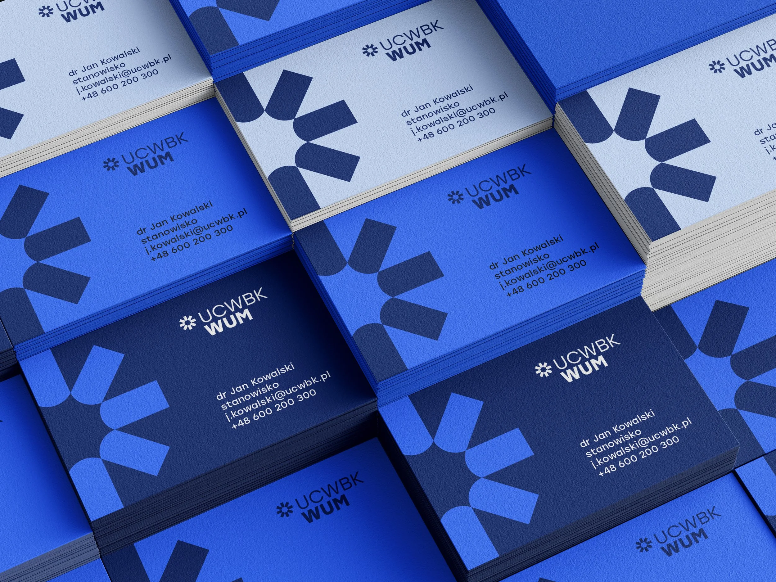 Stacks of business cards for UCW WUM featuring blue shades, a geometric logo, and contact information for Dr. Jan Kowalski.