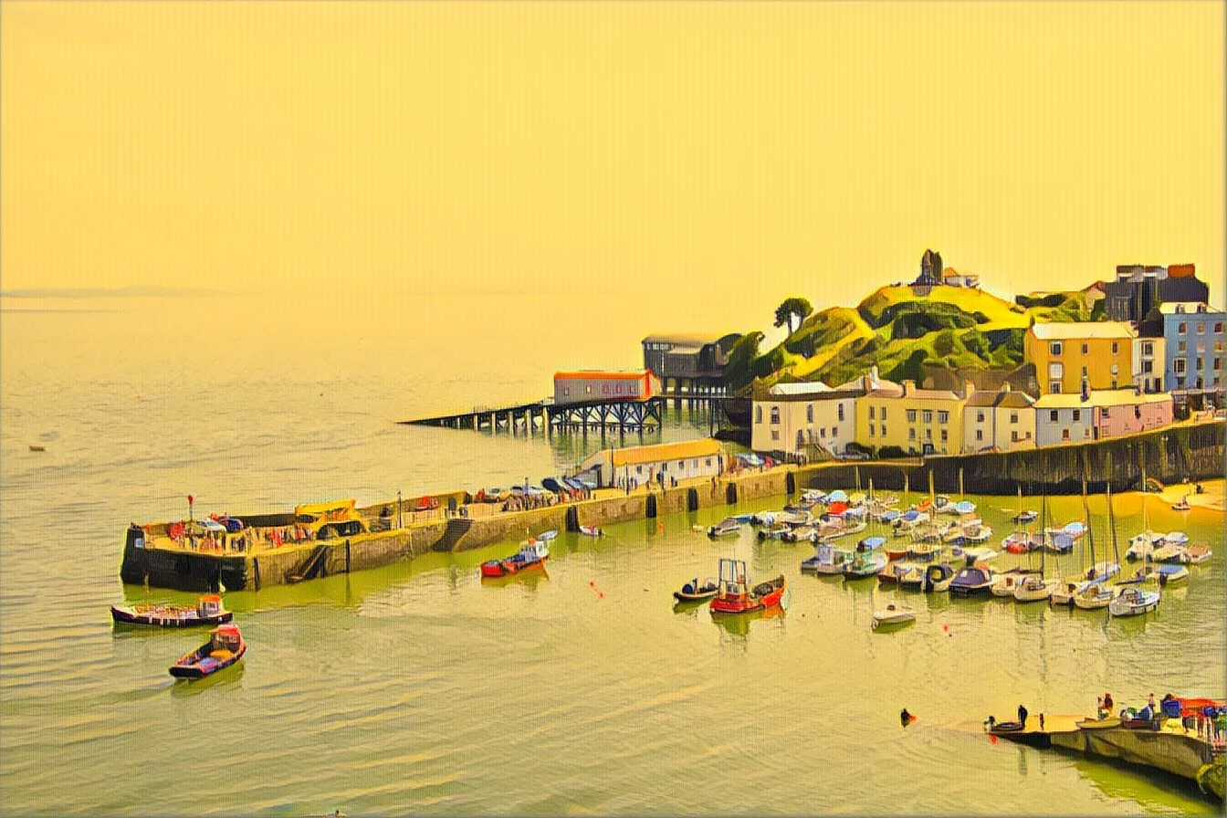 A coastal town with colourful buildings on a hill overlooking a marina filled with small boats and yachts, with a pier extending into the water under a yellow sky. Photography by photographer based in Southam, Warwickshire