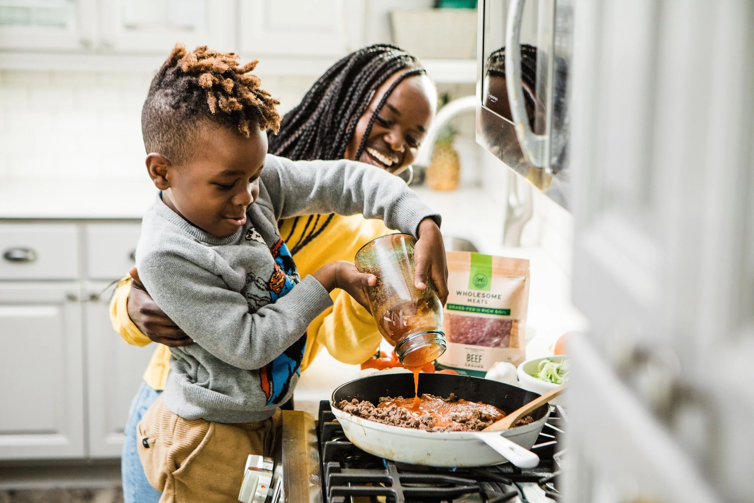 Family cooking with little boy standing over the stove