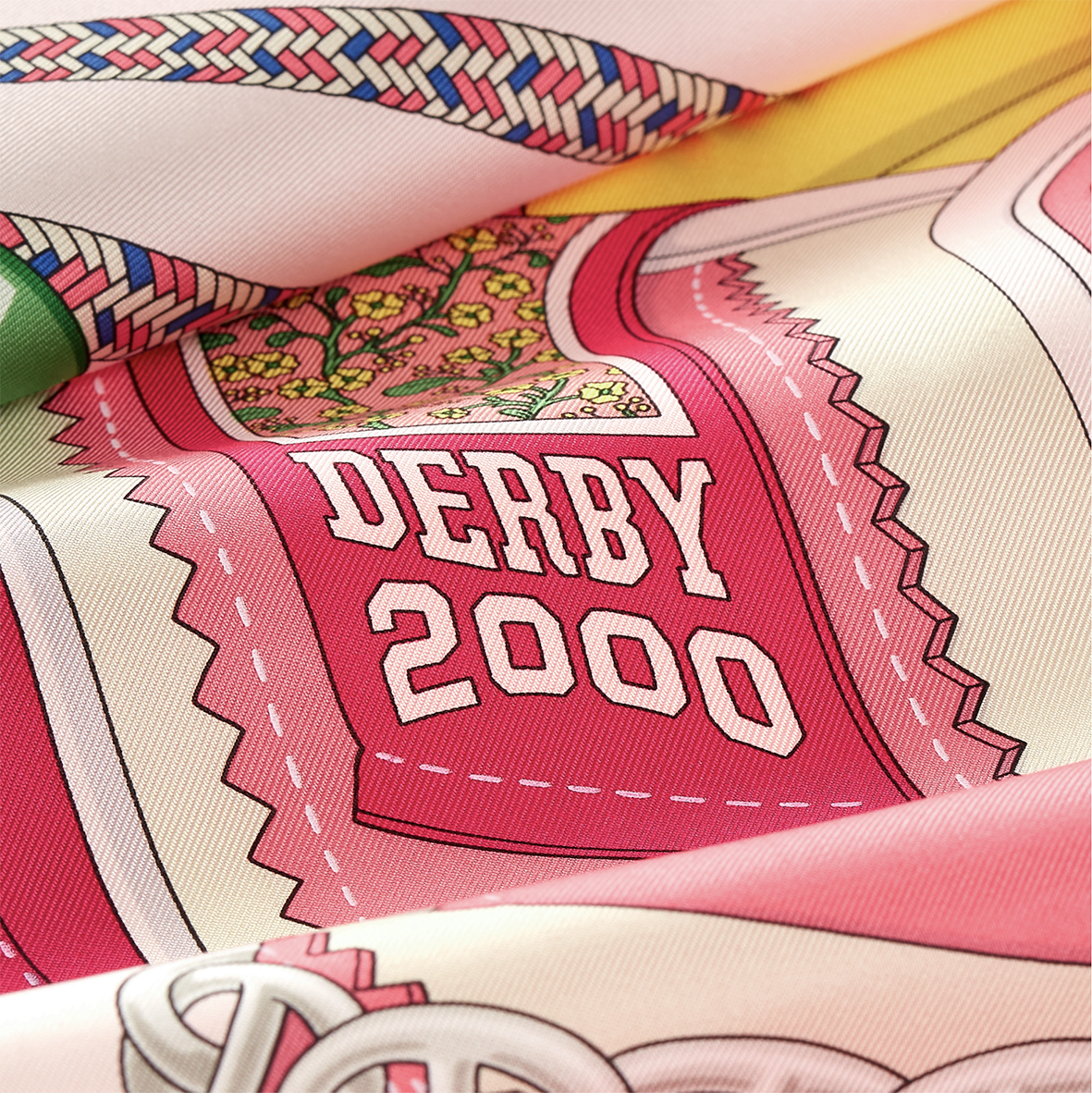 Macro-photographie montrant les détails de l'impression sérigraphiée du texte "DERBY 2000" sur le twill de soie rose fuchsia d'un carré Hermès dessiné par Shane hello.