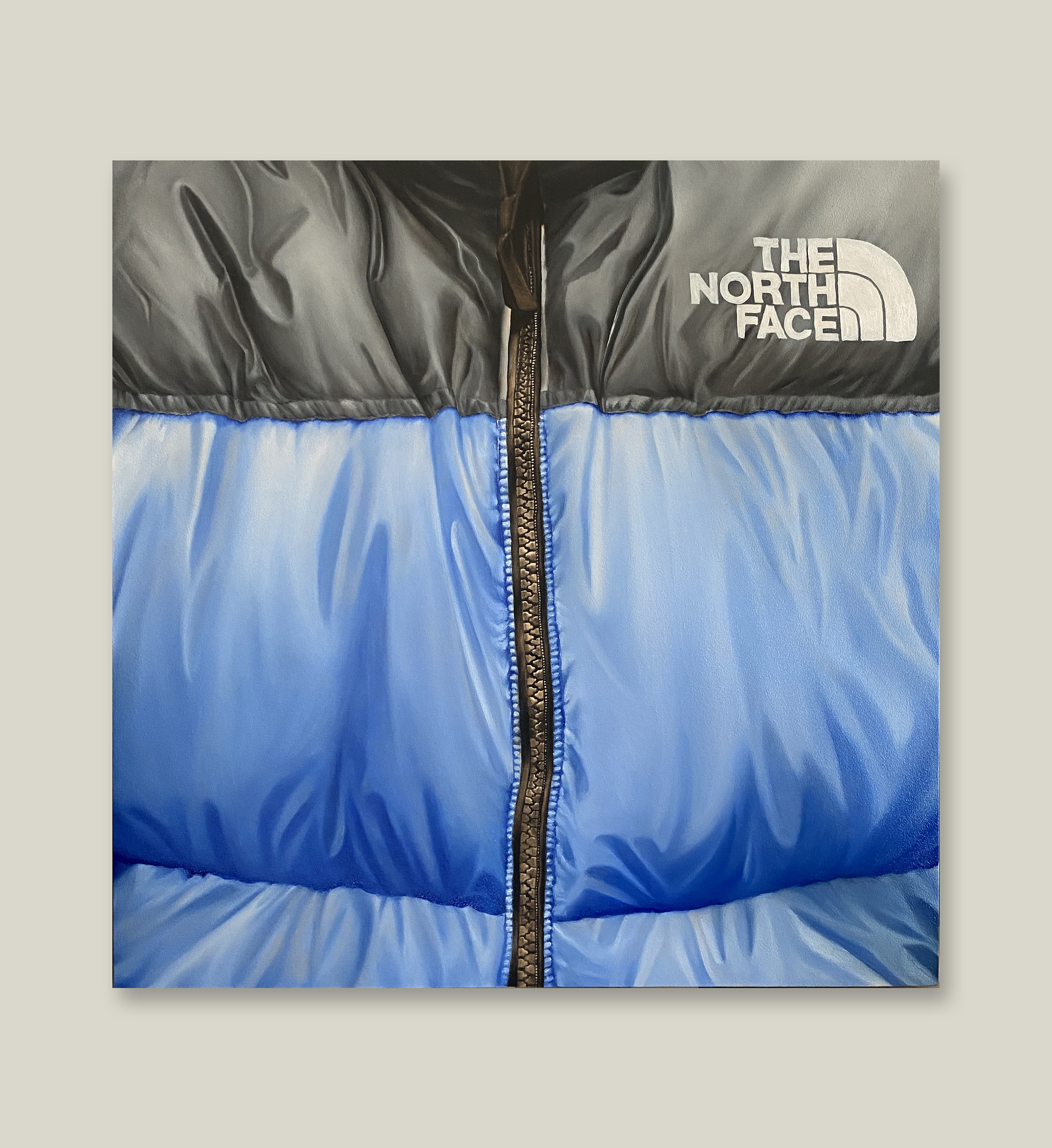 Peinture à l'huile hyperréaliste sur toile par Shane Hello, cadrée en gros plan sur le haut d'une doudoune The North Face Nuptse bleu et noir. L'illustration montre le logo blanc brodé sur l'épaule noire, la fermeture éclair métallique centrale et le