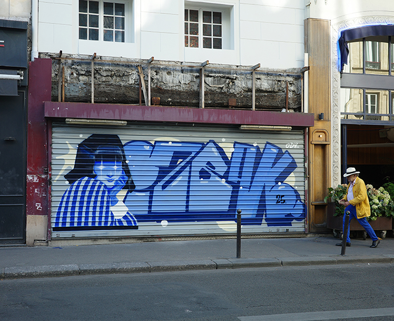 Peinture graffiti en camaïeu de bleus réalisée par Shane Hello sur le rideau de fer métallique d'un magasin parisien. L'œuvre combine à gauche le portrait d'une femme à frange vêtue d'un haut à carreaux avec des étoiles scintillant dans les yeux, et 