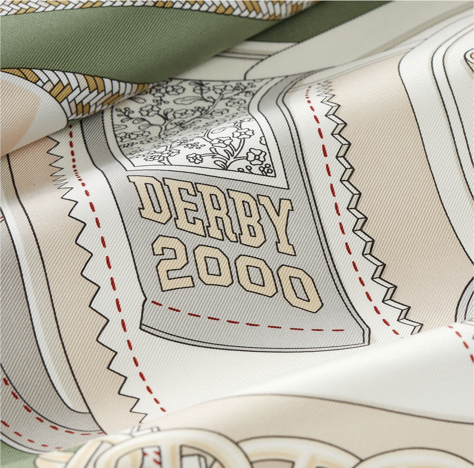 Gros plan sur la soie plissée du carré Hermès "Derby 2000" vert sauge dessiné par Shane hello, montrant la typographie rétro "DERBY 2000", les surpiqûres rouges et la texture du twill de soie.