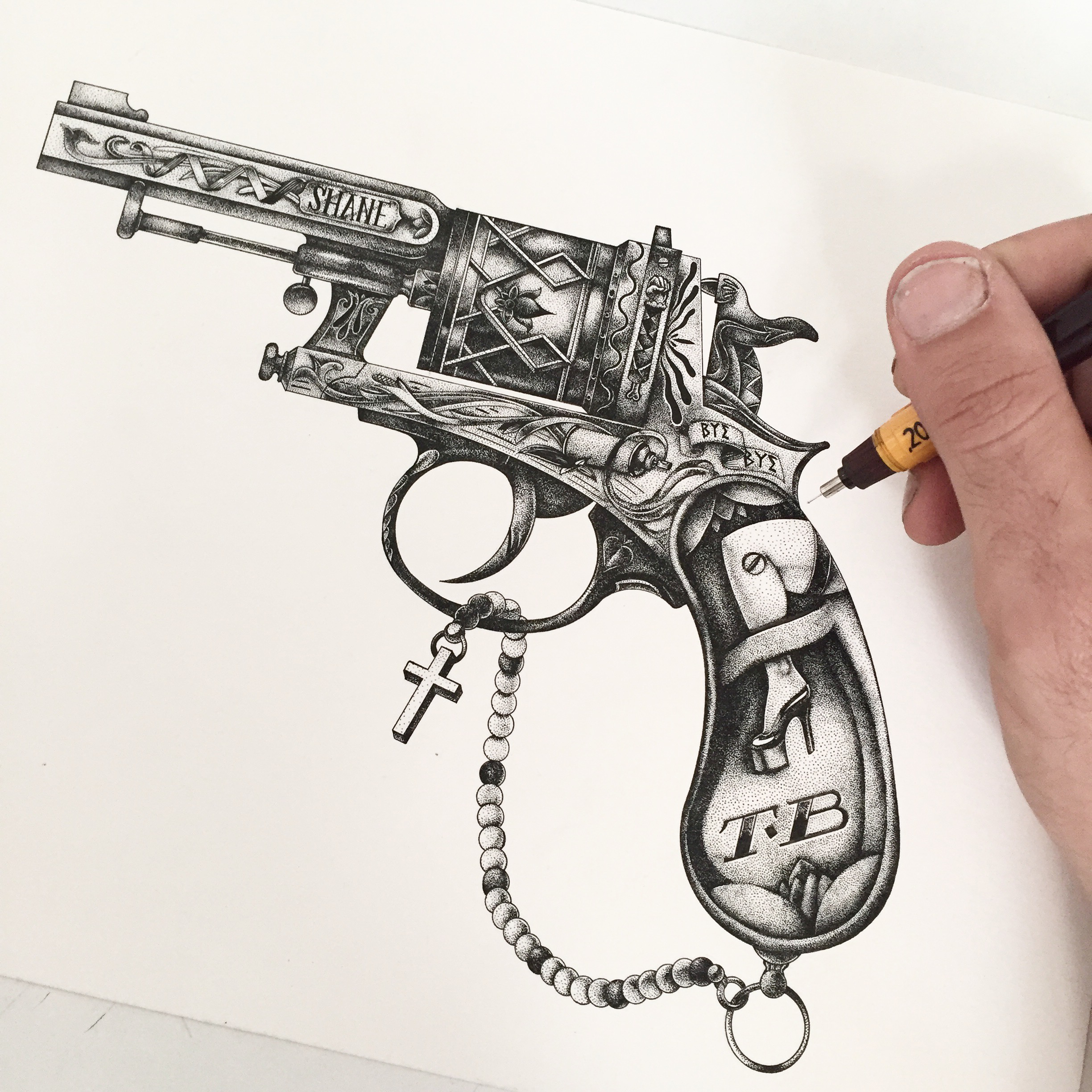 Dessin ultra-détaillé en pointillisme (stippling/dotwork) à l'encre noire par Shane Hello, représentant un revolver vintage ornementé. L'illustration montre le canon gravé du nom « SHANE », un chapelet avec une croix suspendu au pontet, et une crosse