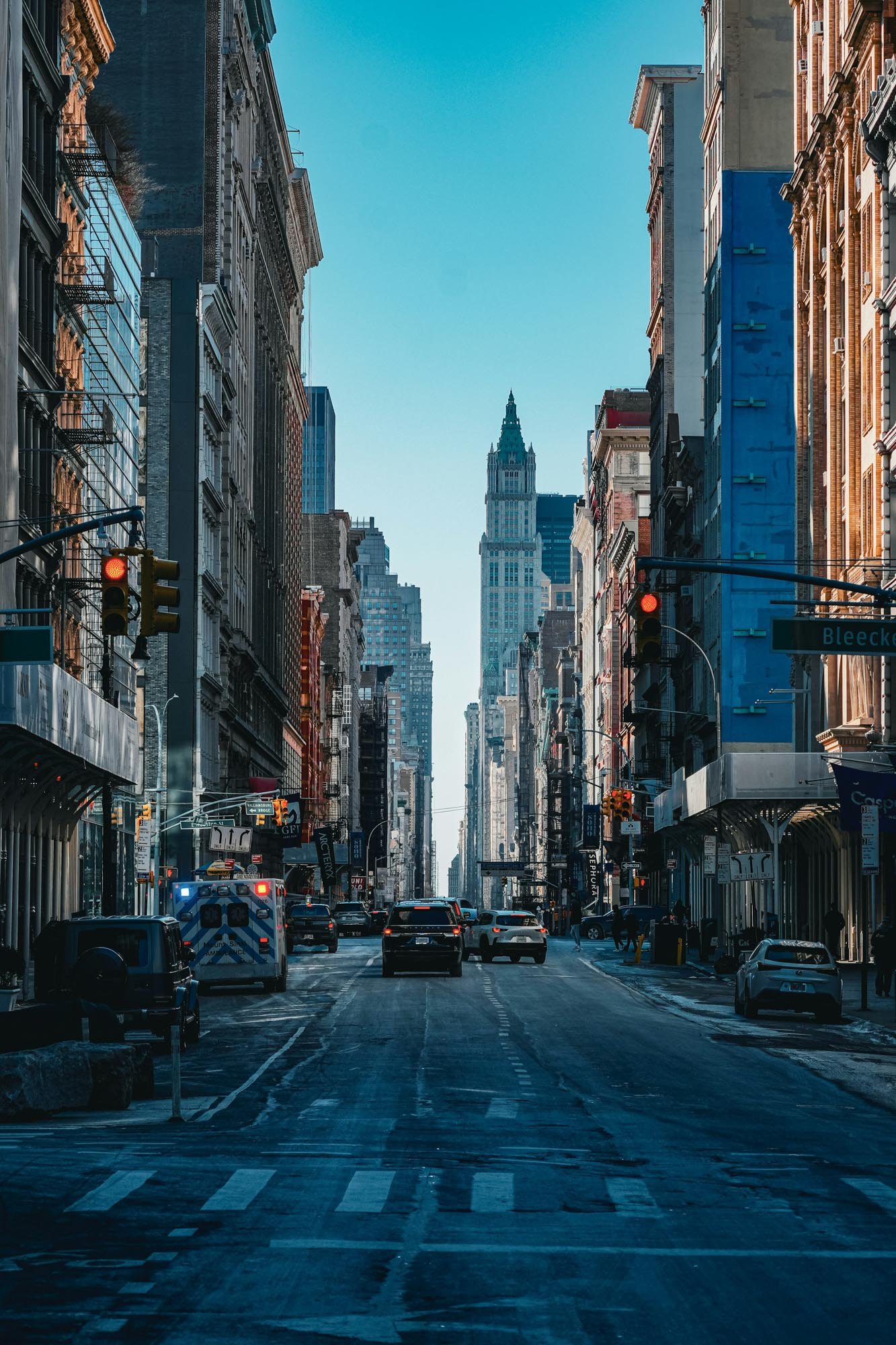 City street scene with tall buildings, cars, and an ambulance, under a blue sky.