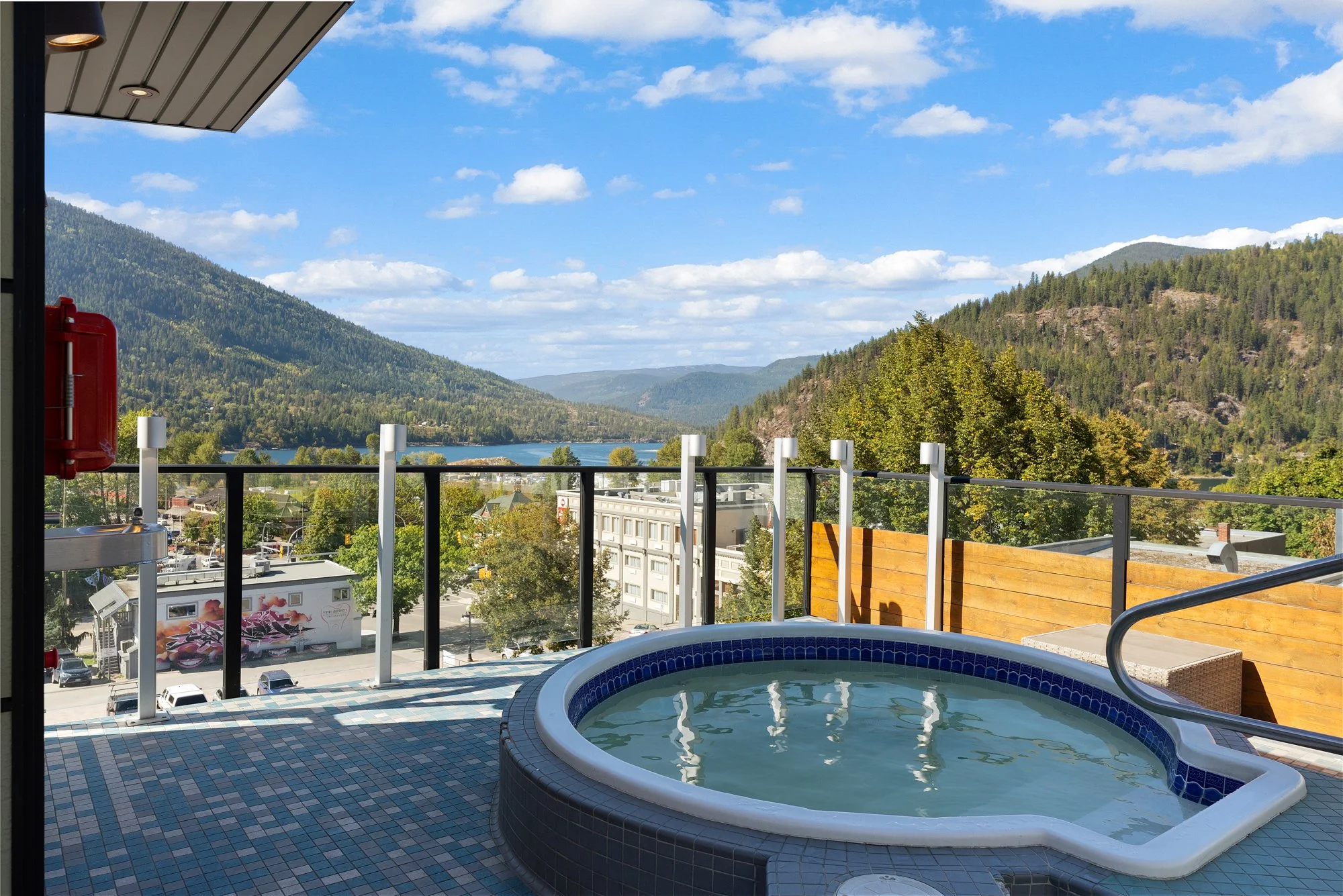A rooftop hot tub overlooks Kootenay Lake on a blue-sky day with clouds.
