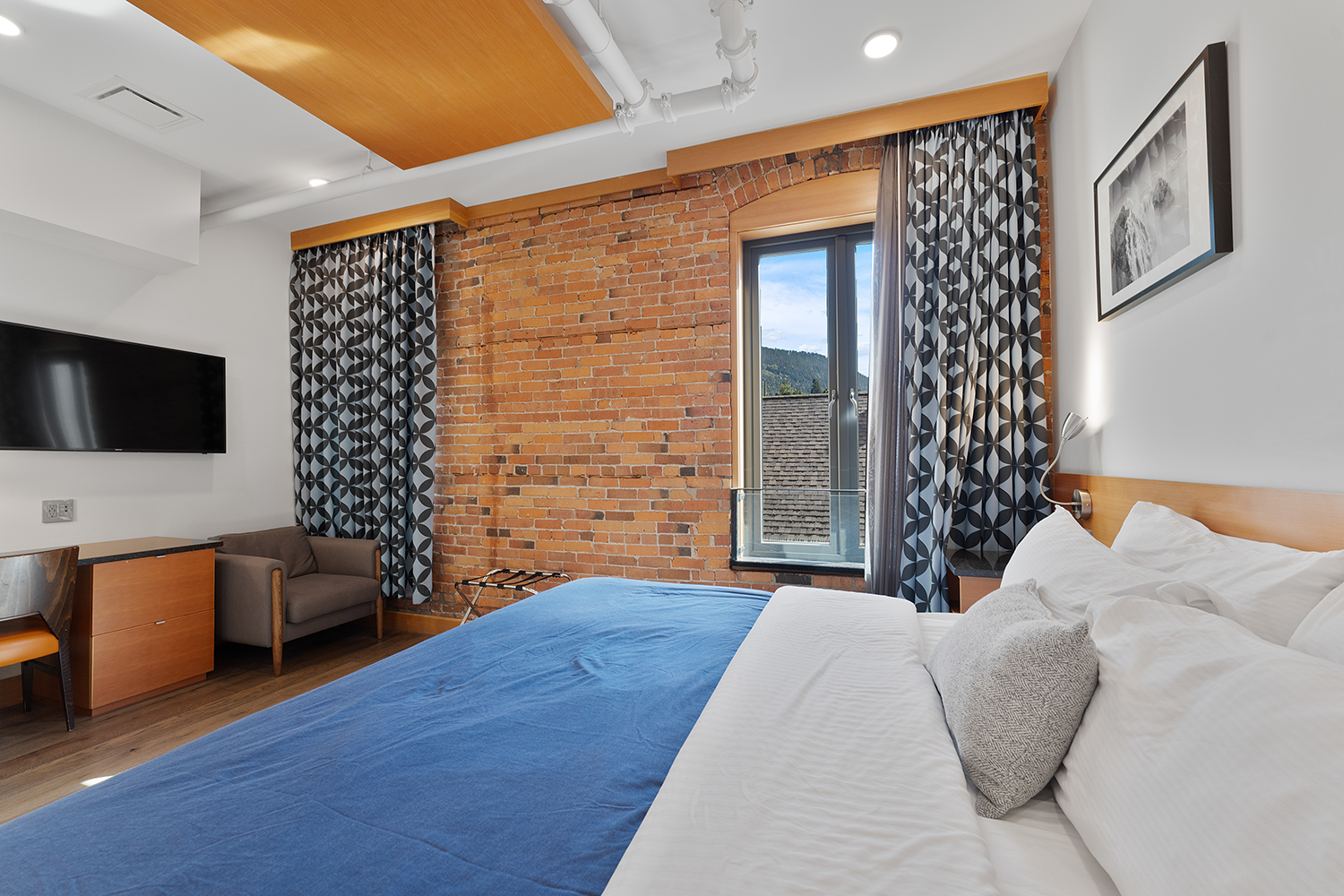 A king-size bed in the Deluxe King room at the Savoy Hotel featuring blue and white bedding and a stunning brick wall.