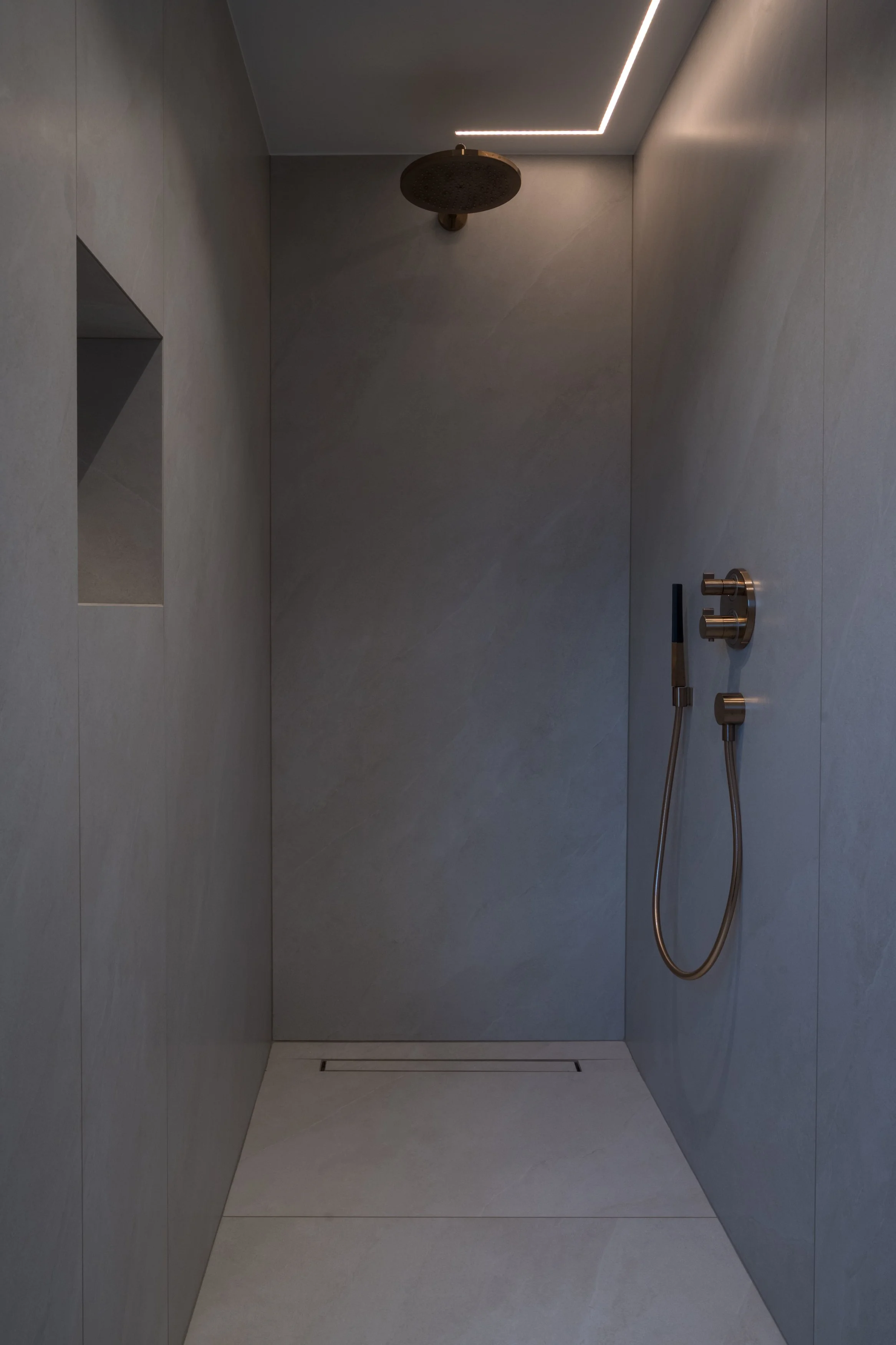 Moderne, minimalistische inloopdouche met muur- en vloertegels in een rustige grijstint, regendouchekop en handdouche