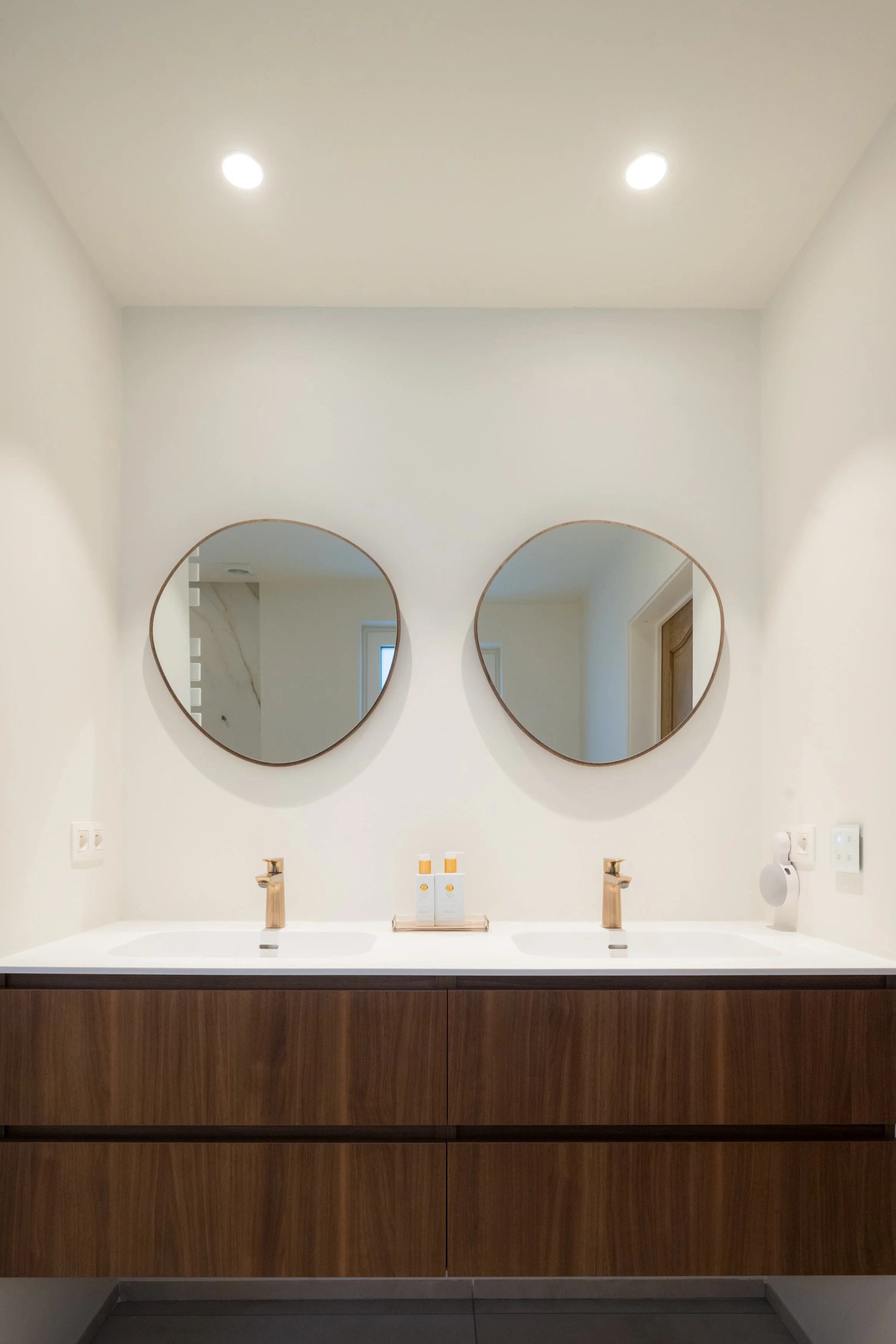 Een badkamer met een dubbele wastafel en twee ronde spiegels boven de wasbakken.