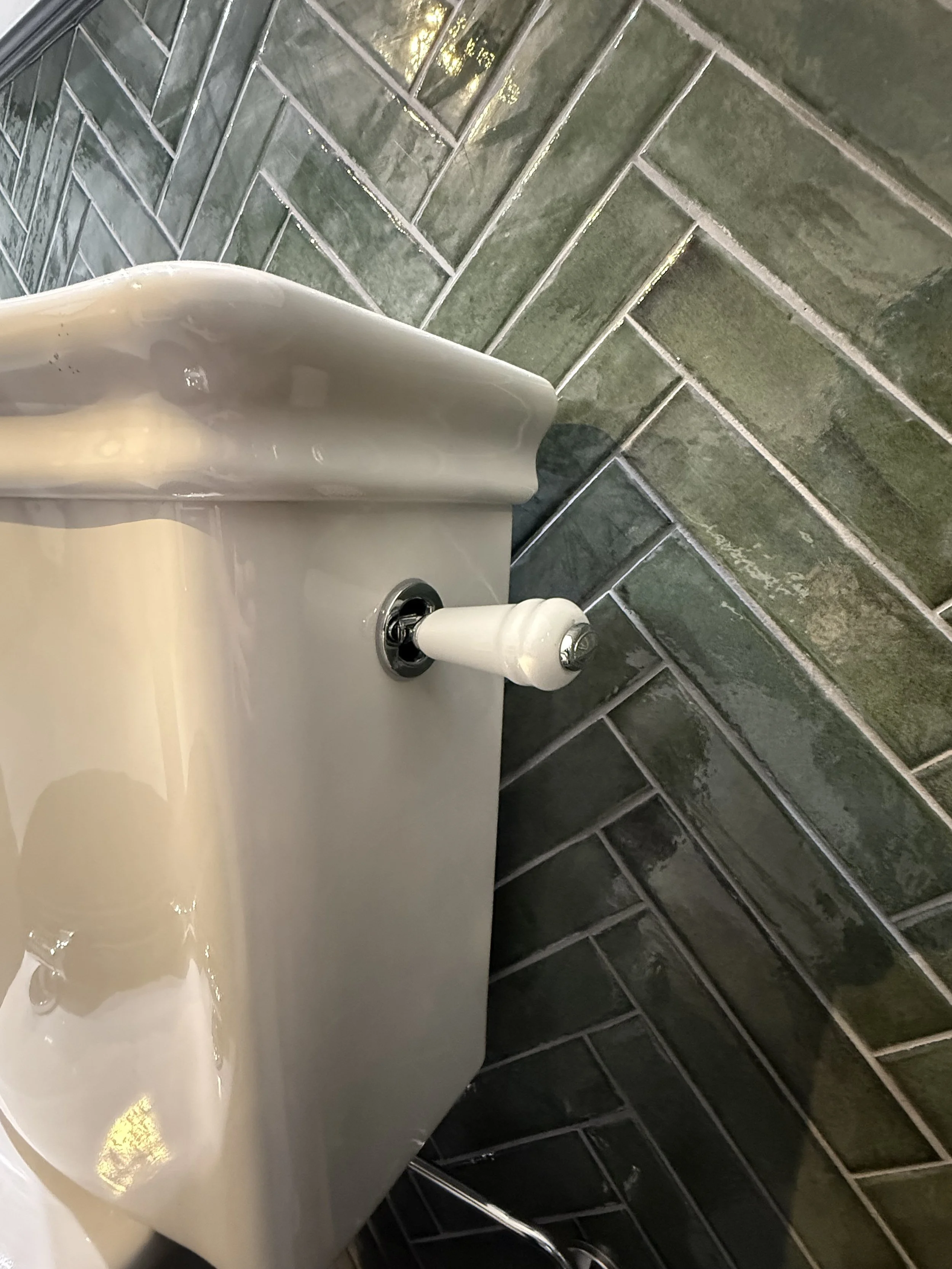 Een witte toiletpot zonder deksel met een witte vulling aan de knop, geplaatst naast een muur met groene keramische tegels.