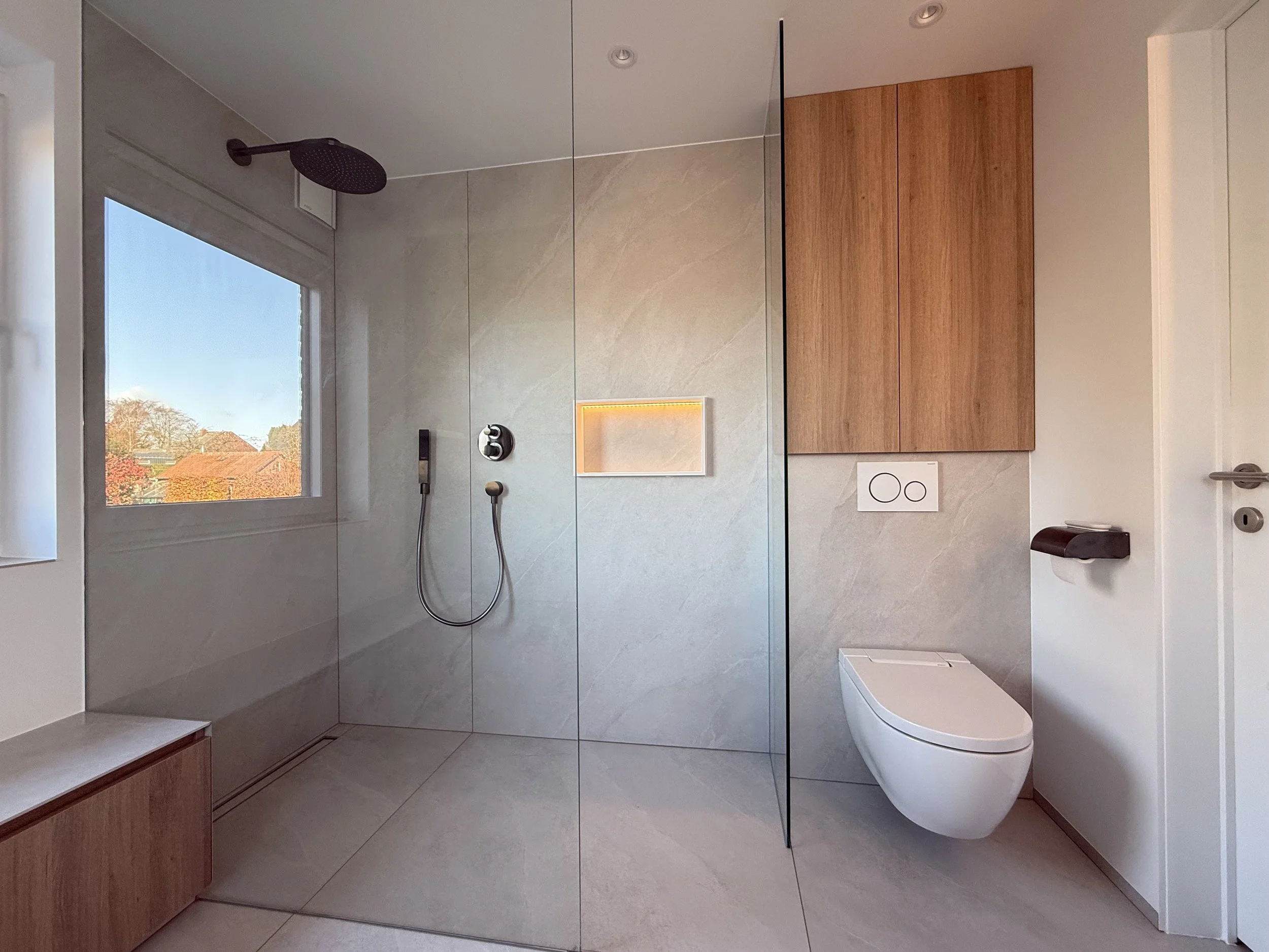 Moderne badkamer met inloopdouche, grote beige tegels, een raam, een wandcloset, houten hangende kast en een toiletrolhouder.