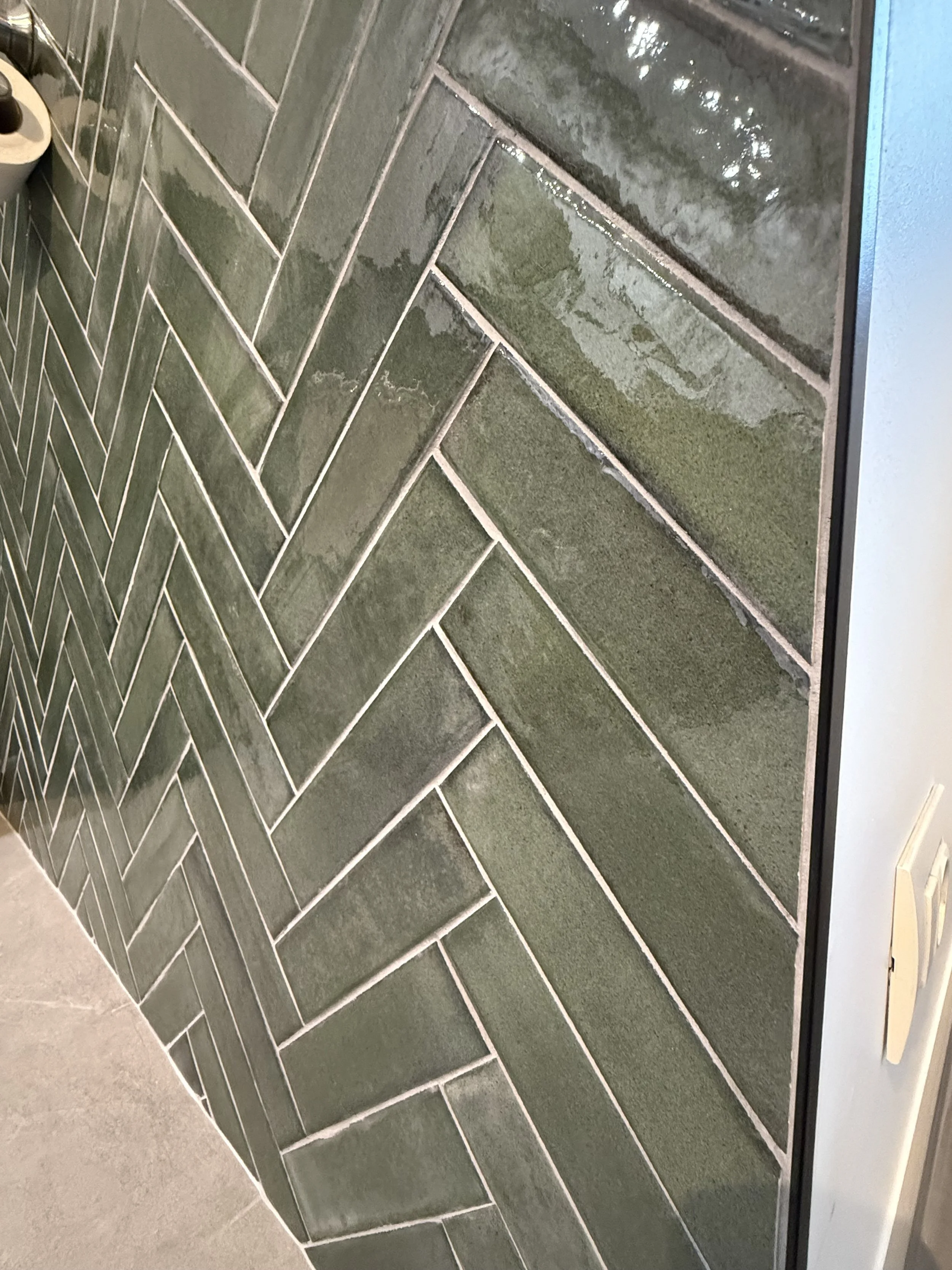 Groene sierklinkers op de muur in visgraatmotief, met een vloer van grijze tegels.