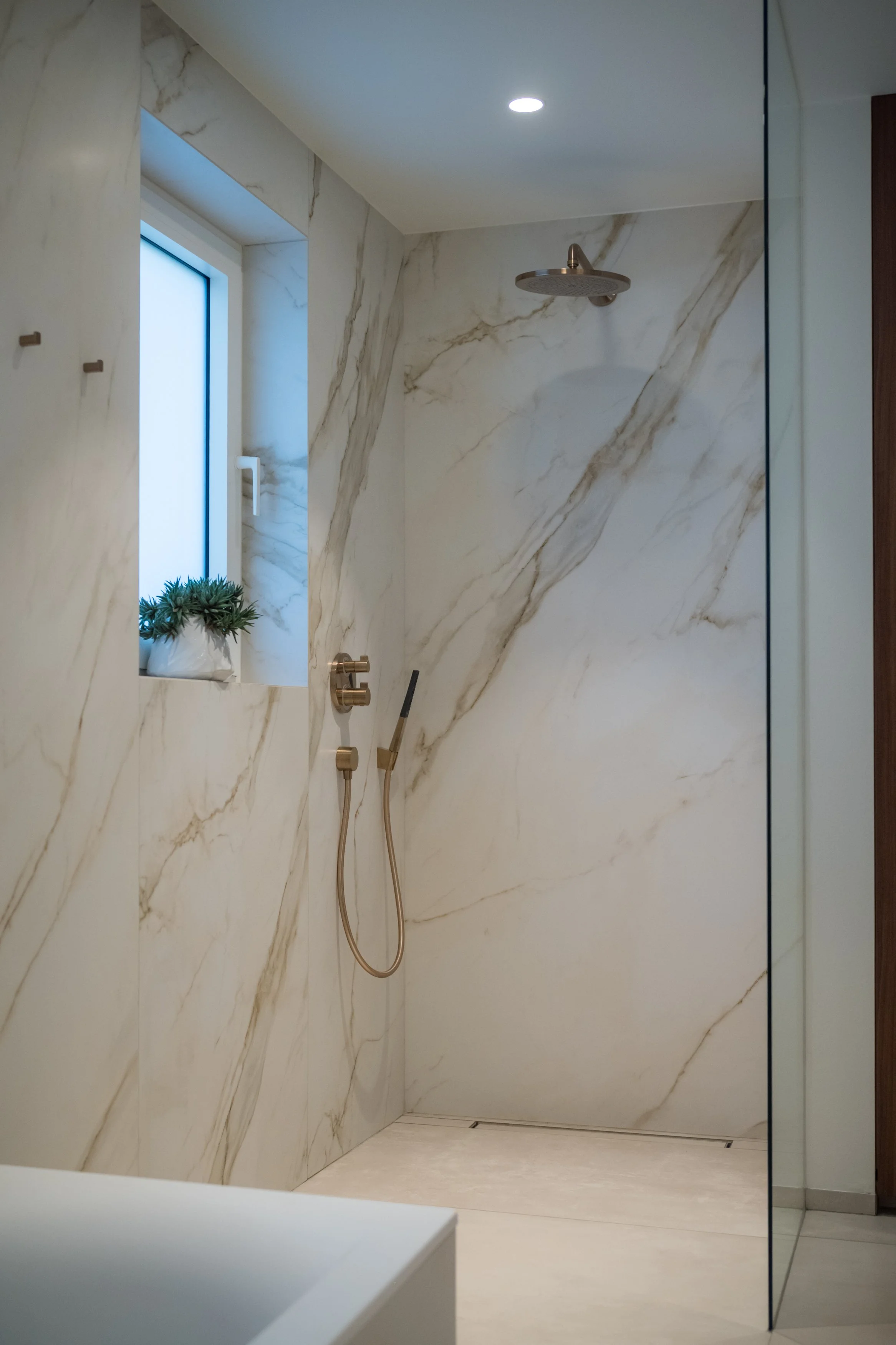 Moderne inloopdouche met marmeren wand en een klein raam met een plantenbakje ervoor.