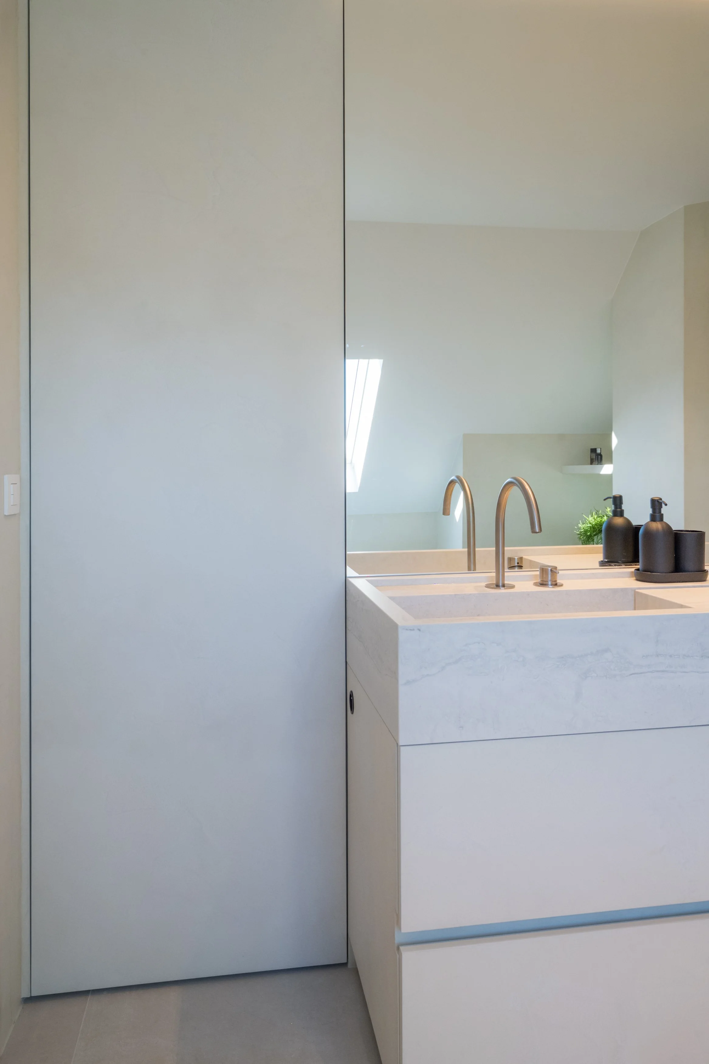 Moderne badkamer met witte wastafel, twee kranen, spiegel en zwart accessoires.