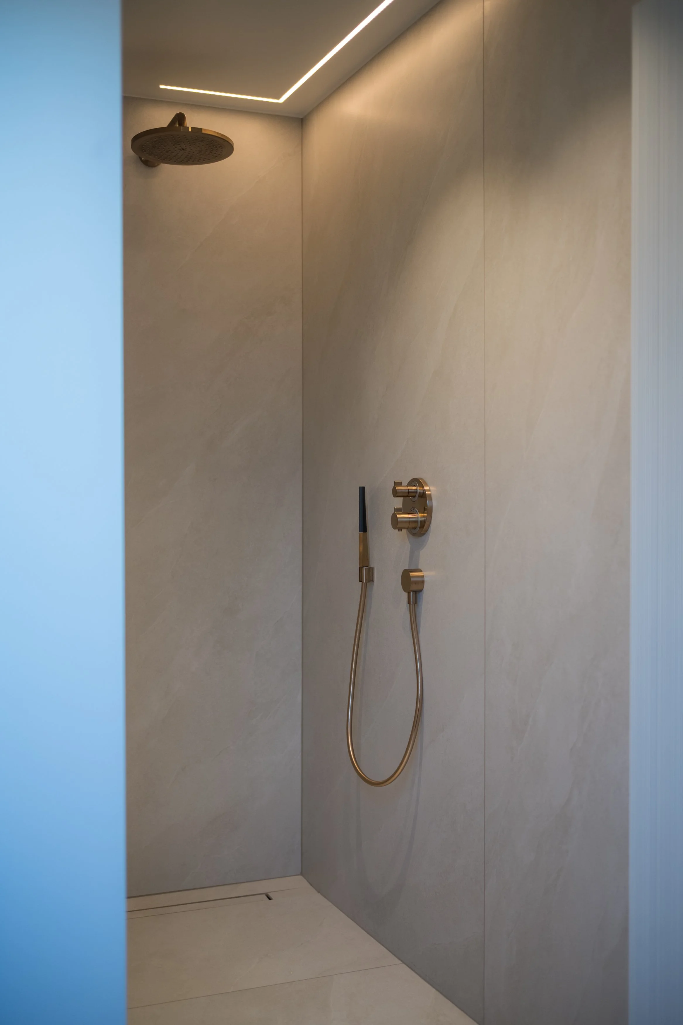 Moderne inloopdouche met rainshower en handdouche in een badkamer met beige marmeren muren.