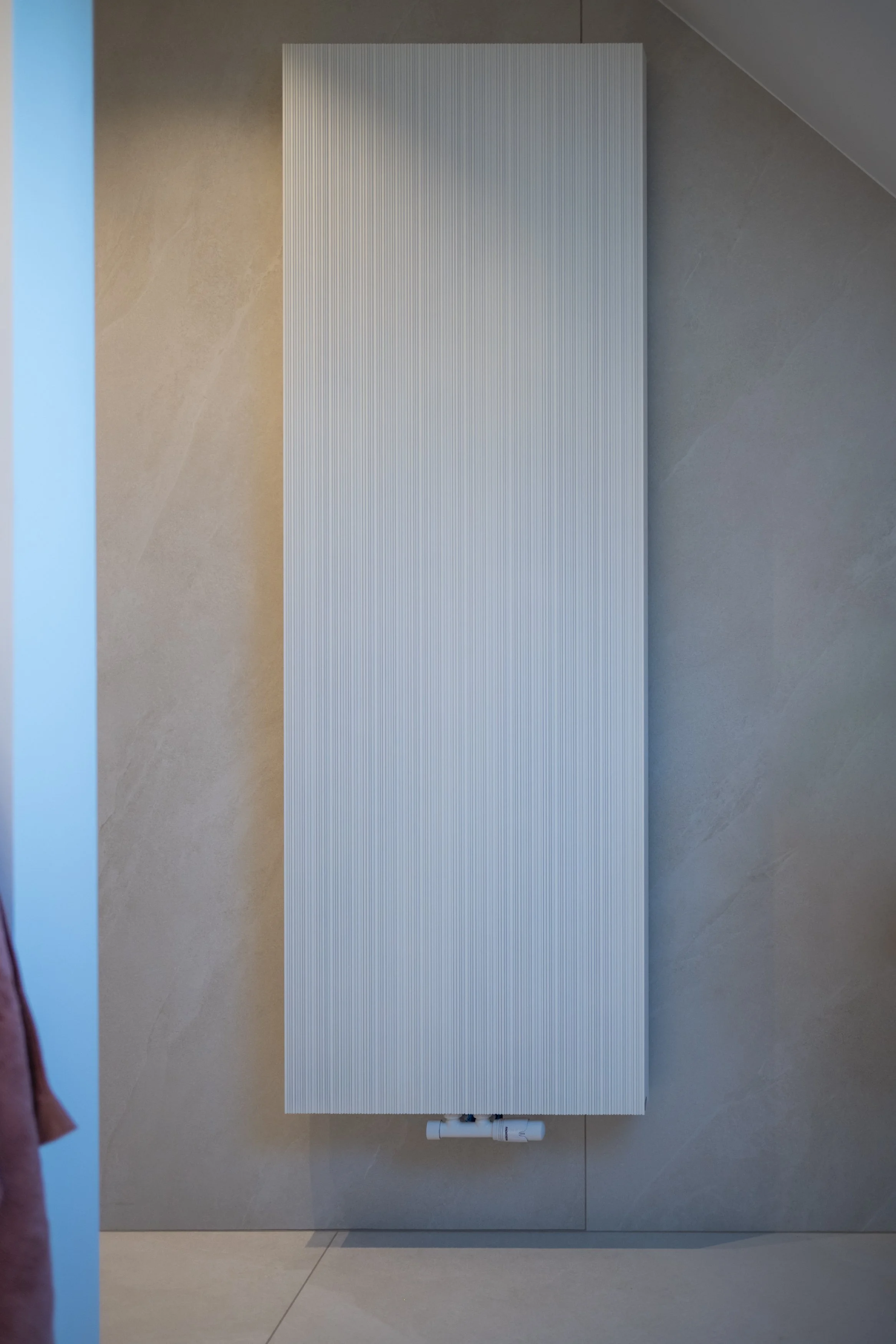 Moderne witte radiator gemonteerd aan een taupe betegelde muur in een woning.