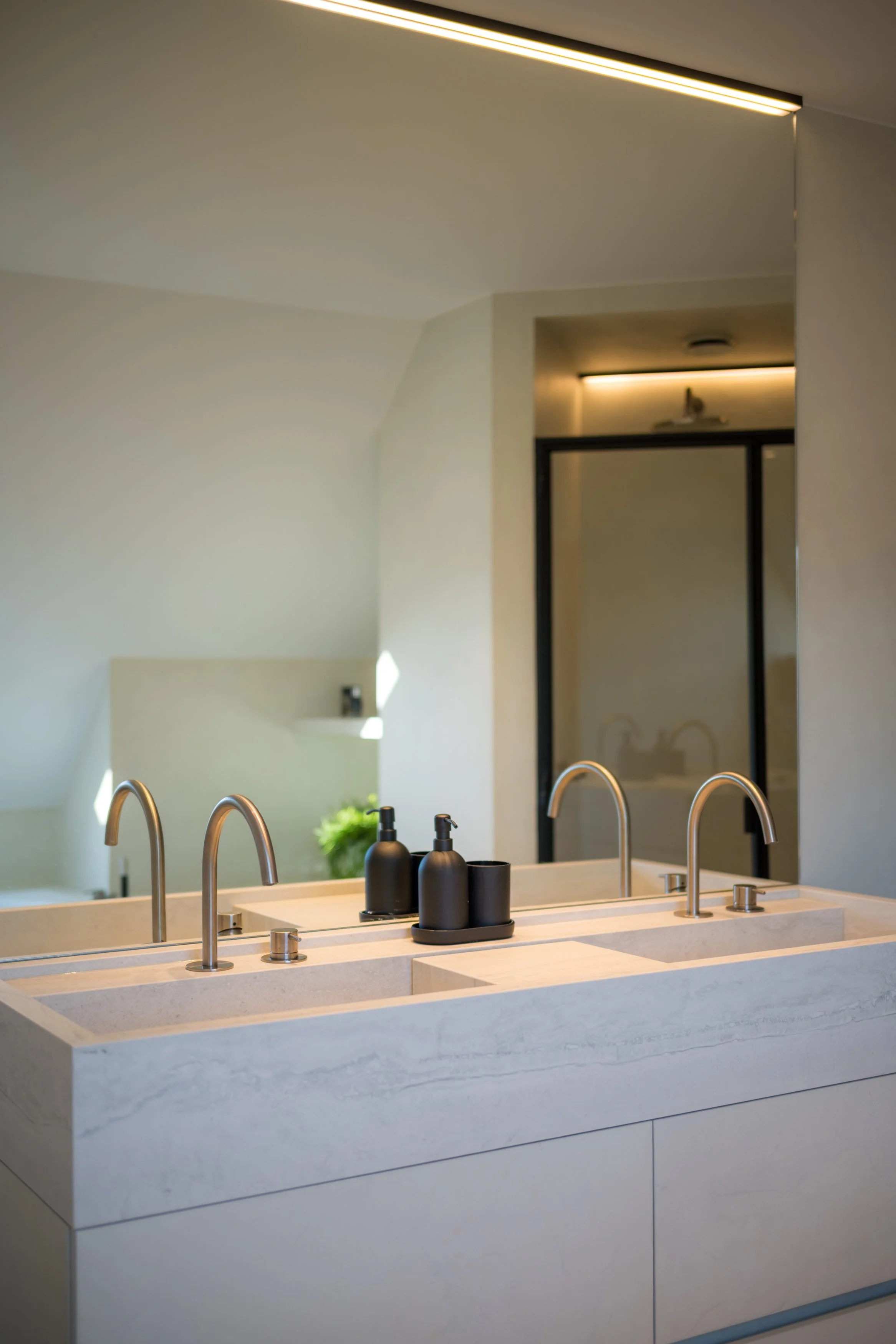 Moderne badkamer met dubbele wastafel en zwarte zeepdispensers, reflectie in spiegel, minimalistisch en licht.