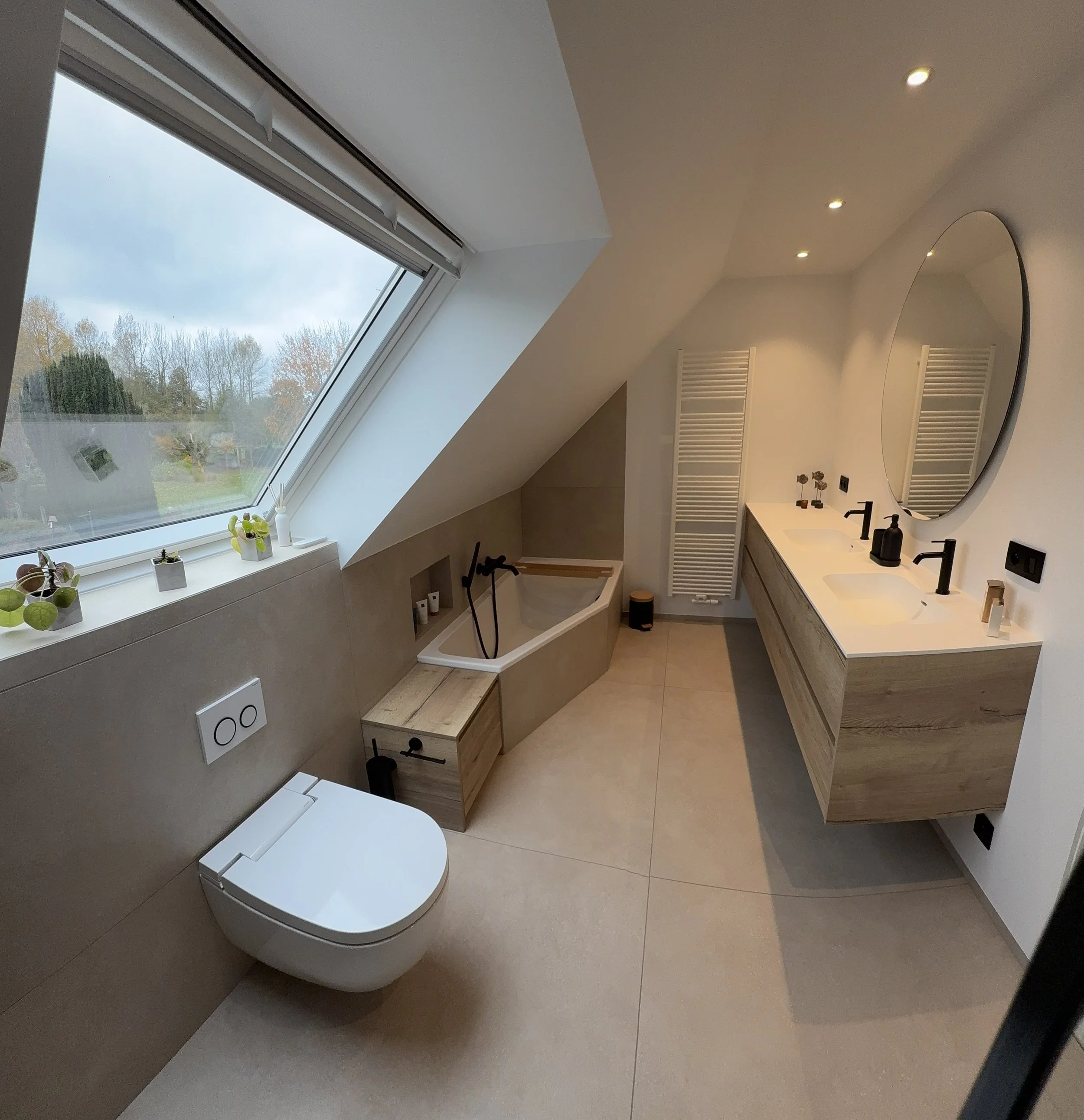 Moderne badkamer met dakraam, ligbad, grote spiegel, dubbele wastafel en witte radiator