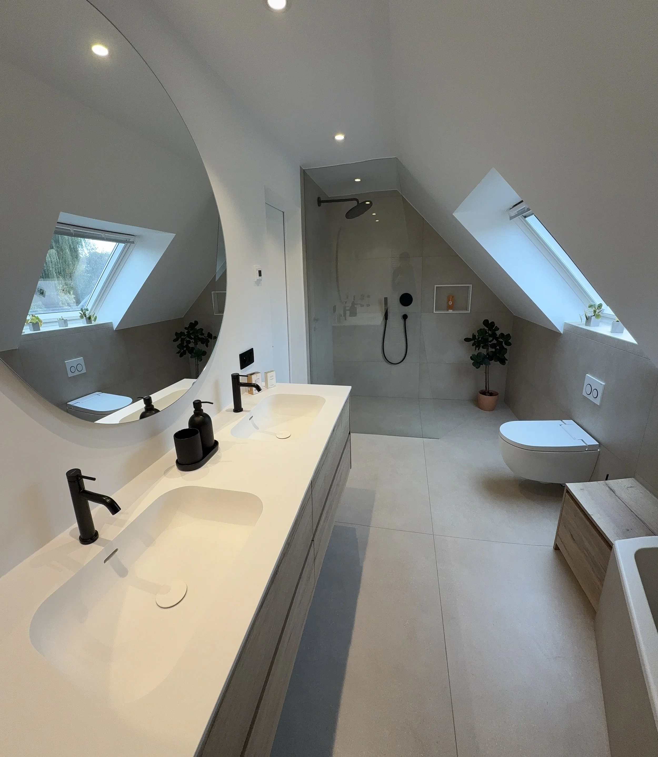 Een moderne badkamer met een dubbele wastafel, grote spiegel, inloopdouche met glazen wand, toilet, ramen met uitzicht en wandplanken met planten.