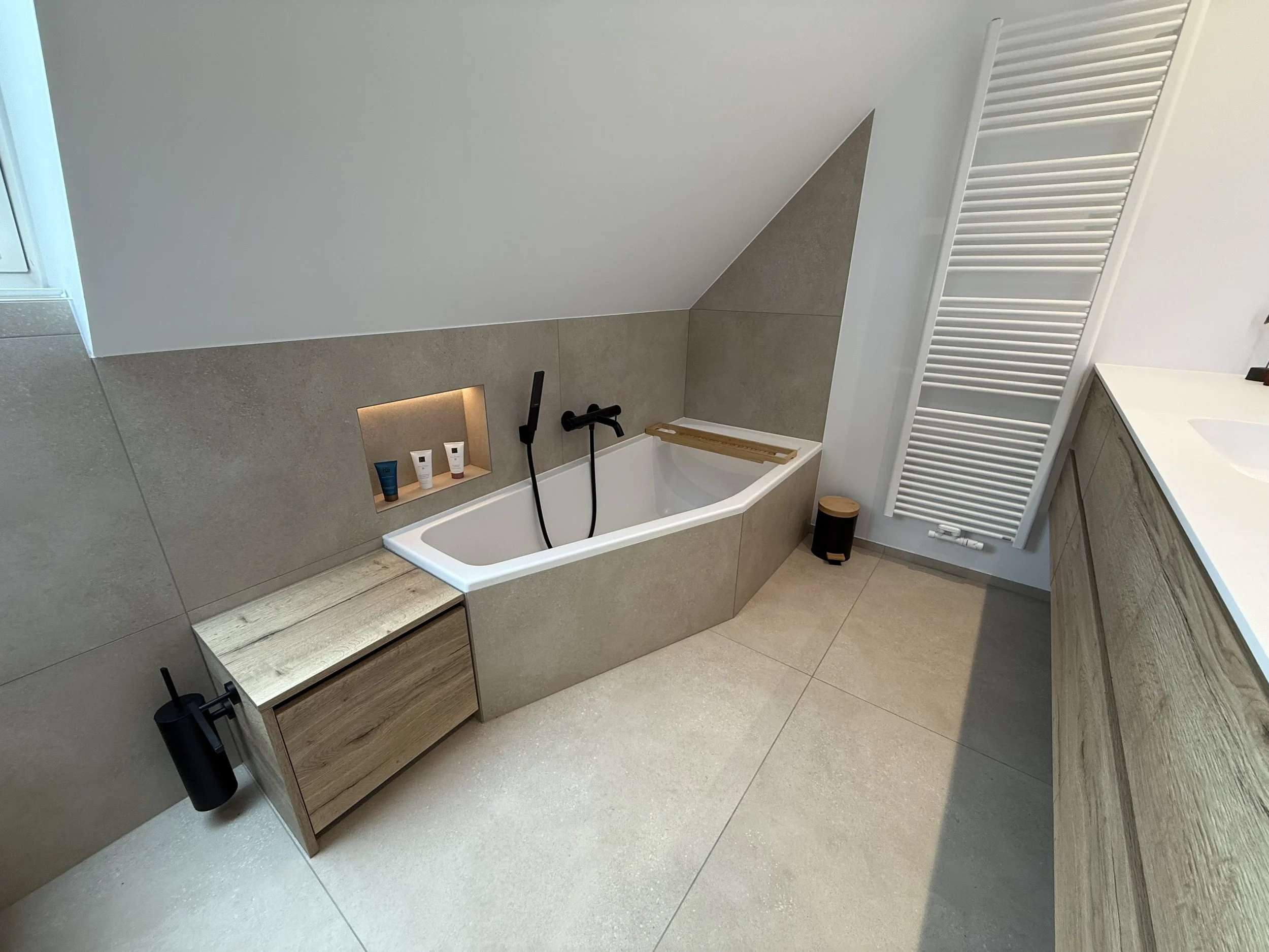 Badkamer met een ingebouwde badkuip, houten kast, witte radiator en wastafel met houten onderkast.