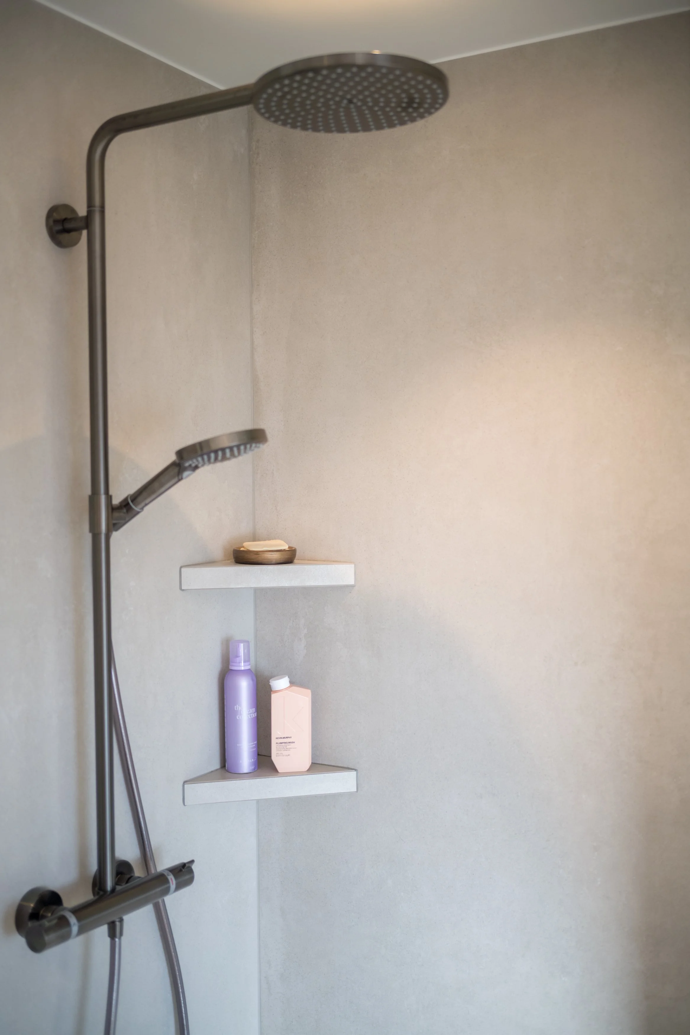 Moderne inloopdouche met een regenbad en een handdouche, witte wandplanken met verzorgingsproducten.